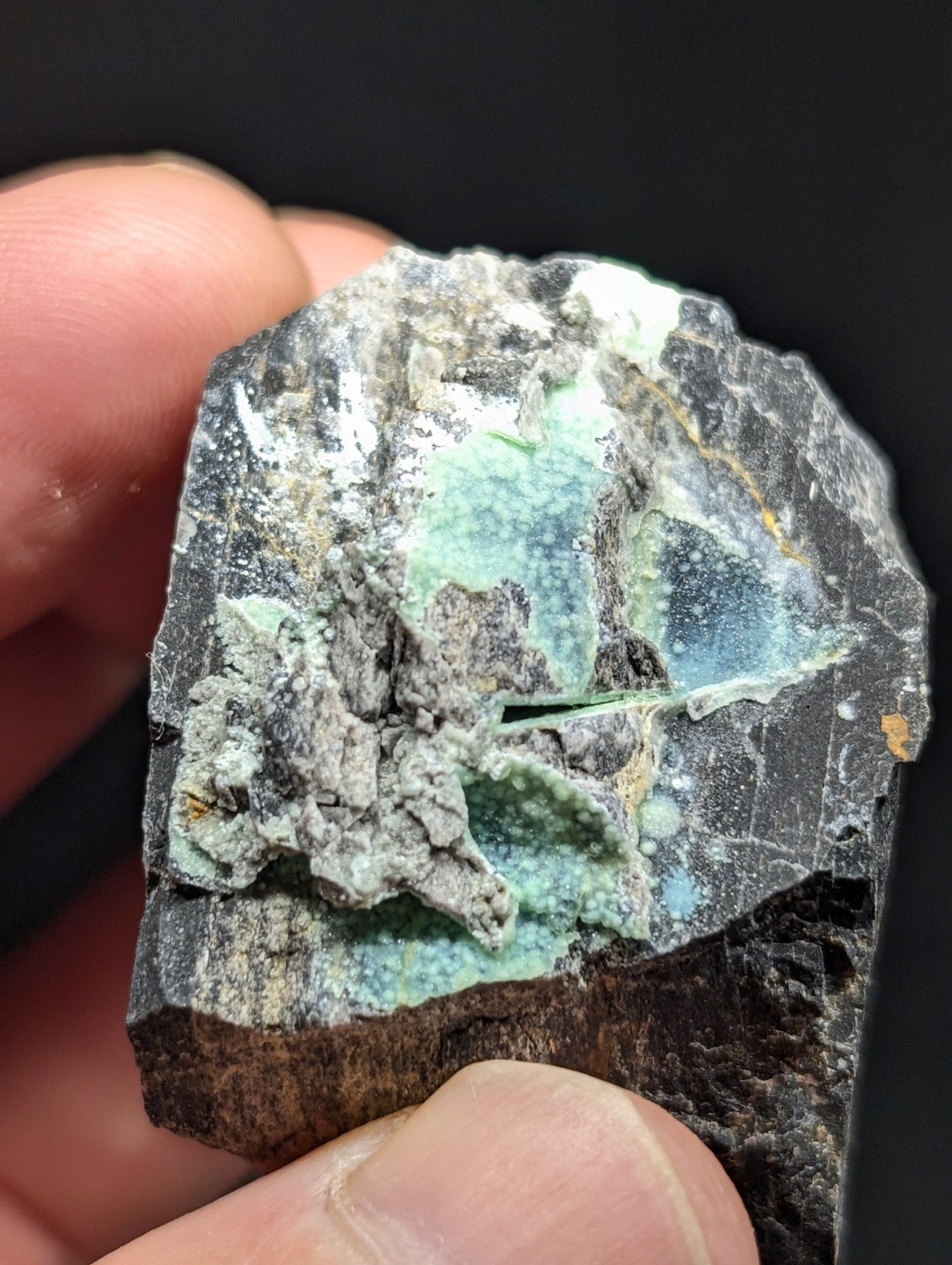 A rough, irregularly shaped mineral specimen with a dark gray matrix and vibrant turquoise-green veining.
