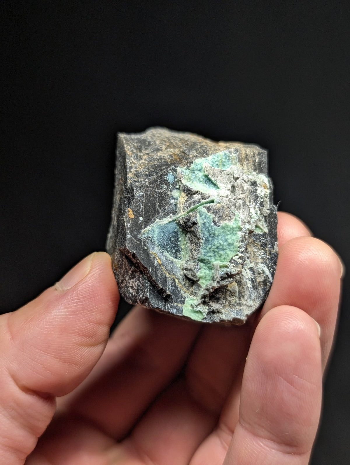 A rough, irregularly shaped mineral specimen with a dark gray matrix and patches of vibrant green patina.