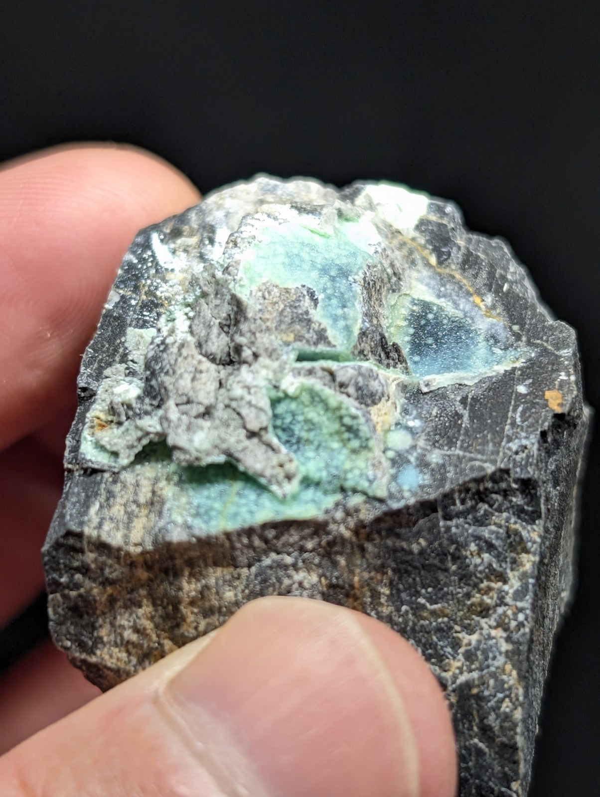 A rough, dark gray rock with patches of vibrant turquoise mineral inclusions.