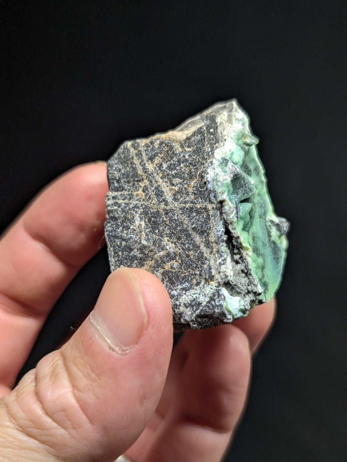 A rough, irregularly shaped piece of green mineral with a dark gray matrix and visible crystalline textures.
