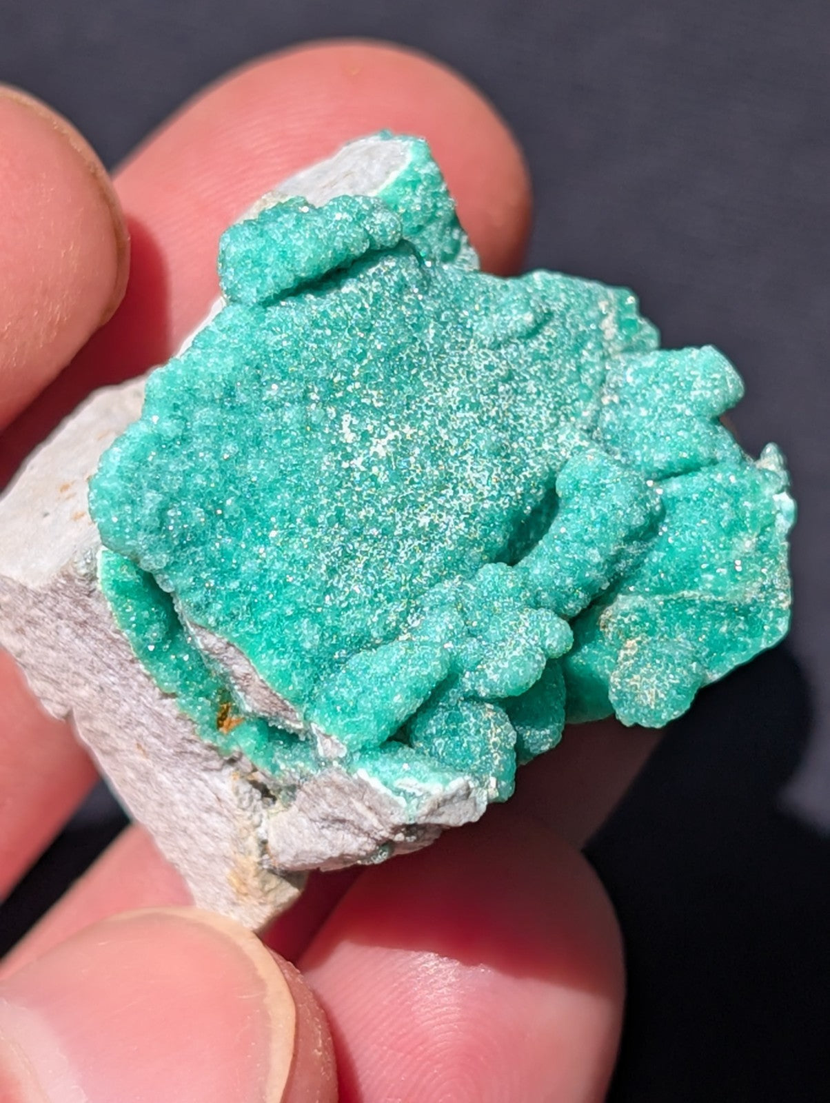A vibrant turquoise-green mineral specimen with a crystalline, textured surface and white speckles.