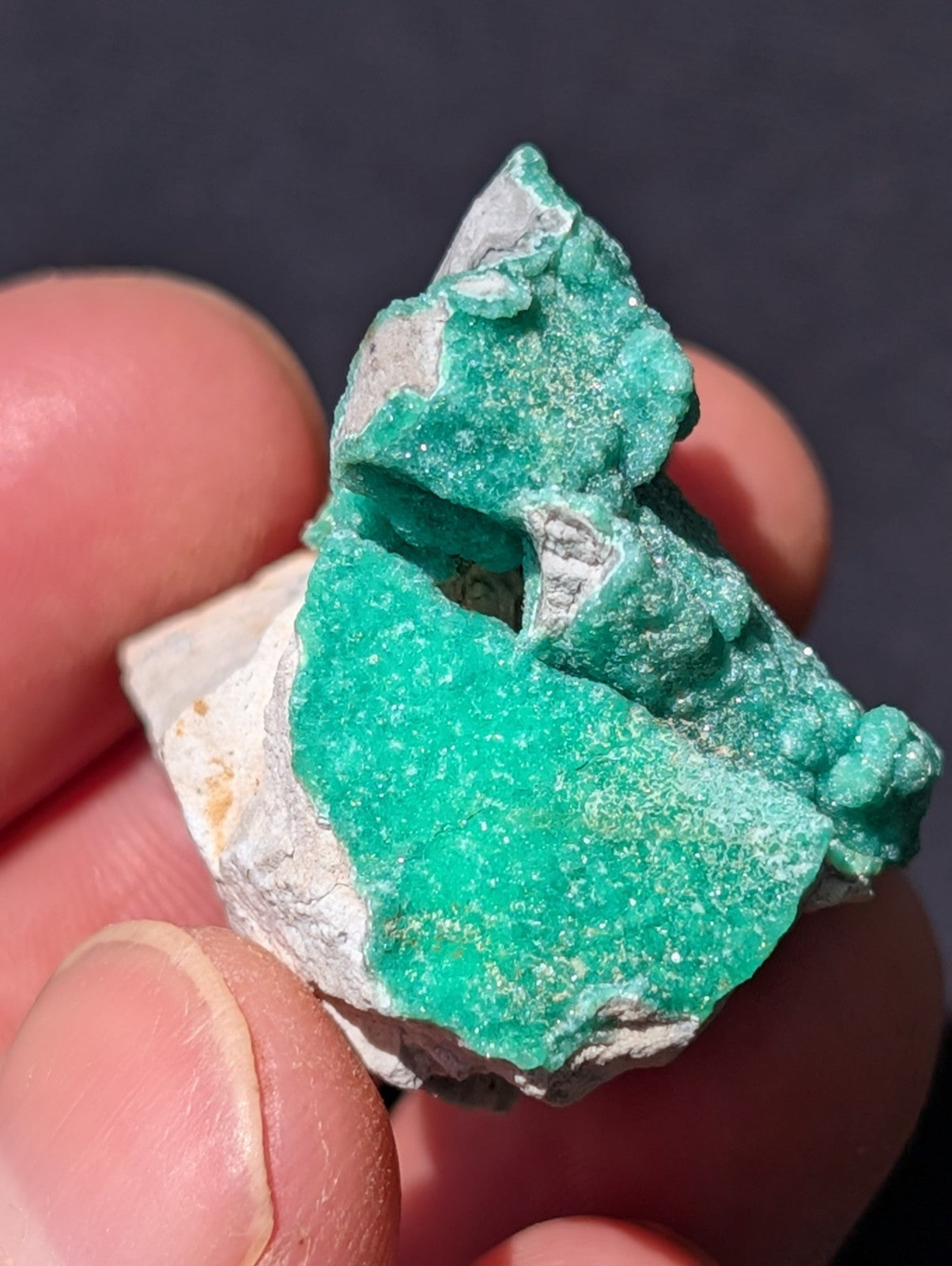 A vibrant green mineral specimen with a crystalline texture, partially embedded in white matrix rock.
