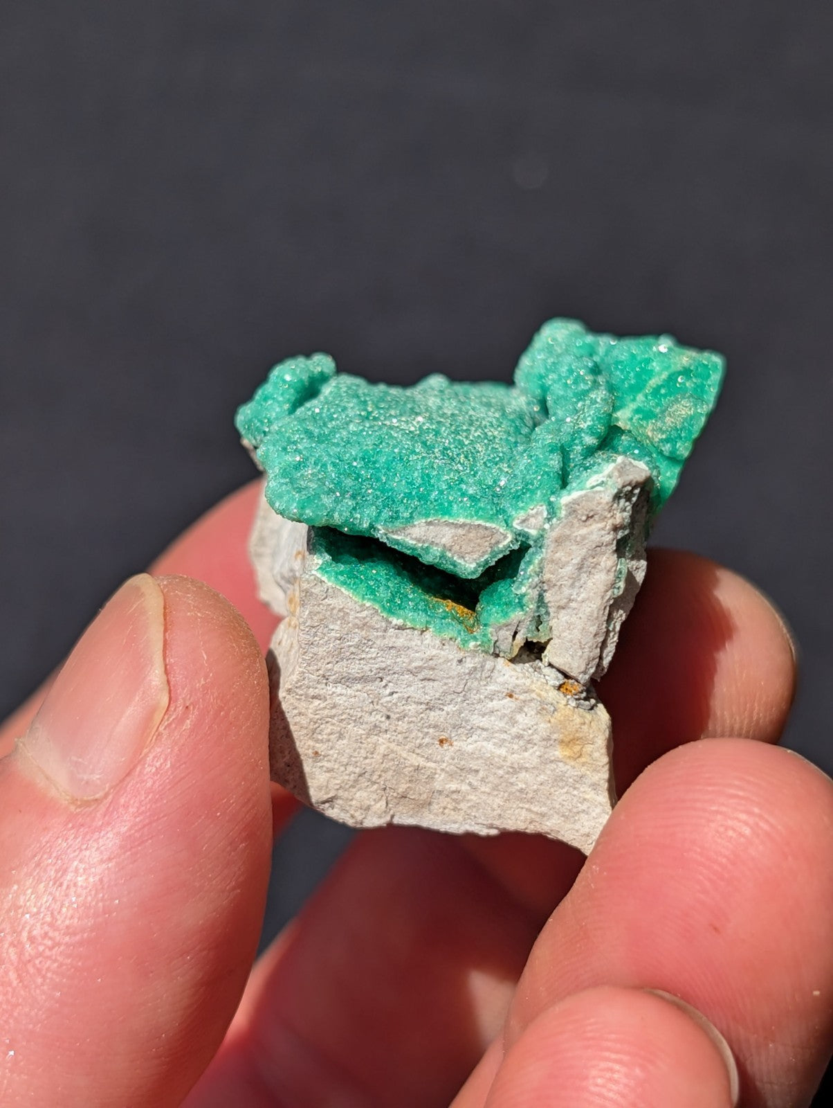A vibrant green, crystalline mineral specimen with a rough, jagged surface and white matrix.