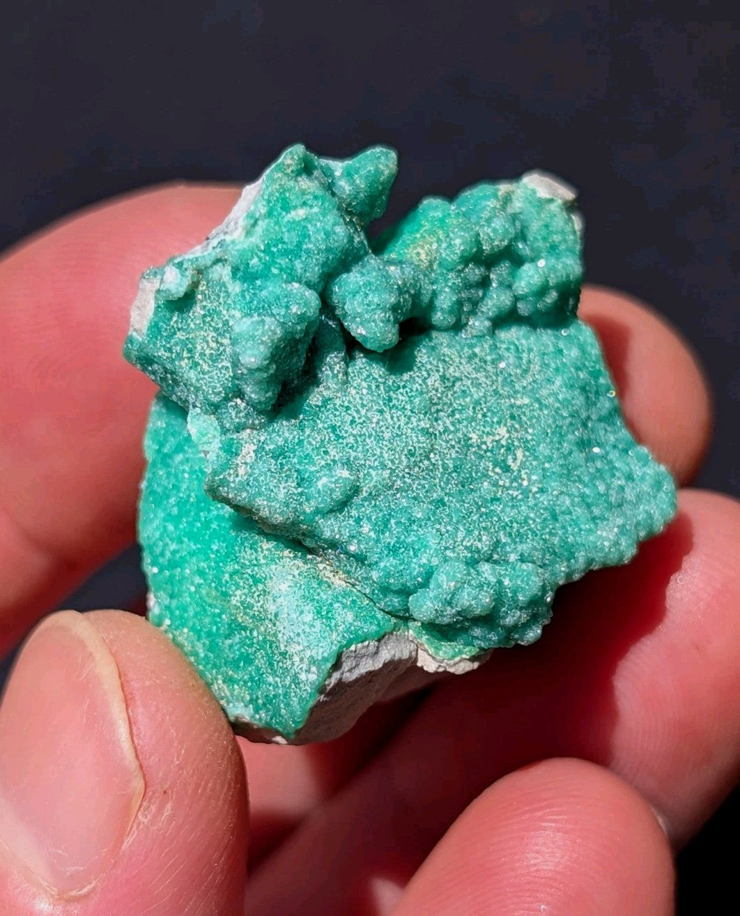A vibrant green, naturally occurring mineral specimen with a rough, textured surface and white crystalline patches.