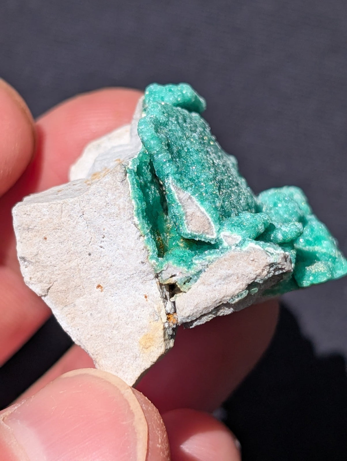 A vibrant green, crystalline mineral specimen with a rough, textured surface nestled against a pale gray rock matrix.