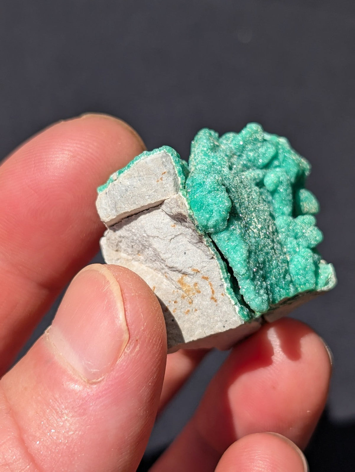 A vibrant green, crystalline mineral specimen with a rough, textured surface contrasting against its pale gray rock matrix.