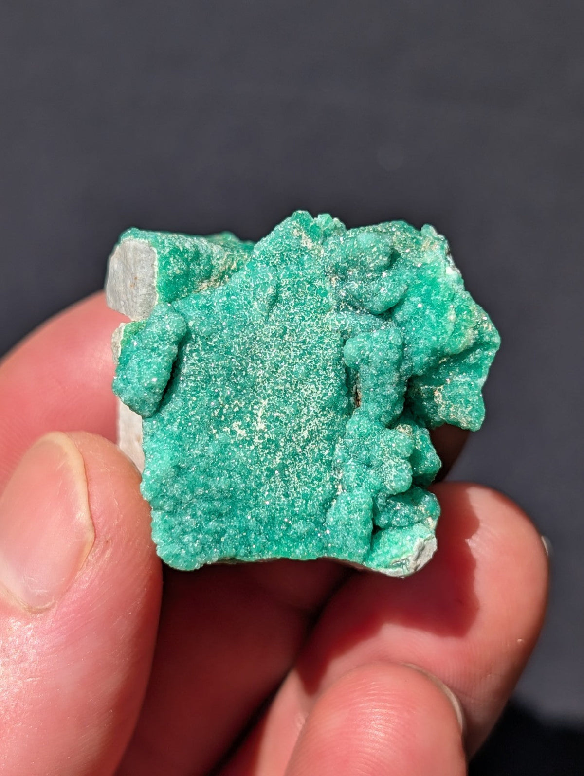 A vibrant green, rough-textured mineral specimen with a crystalline, irregular surface and some white speckles.