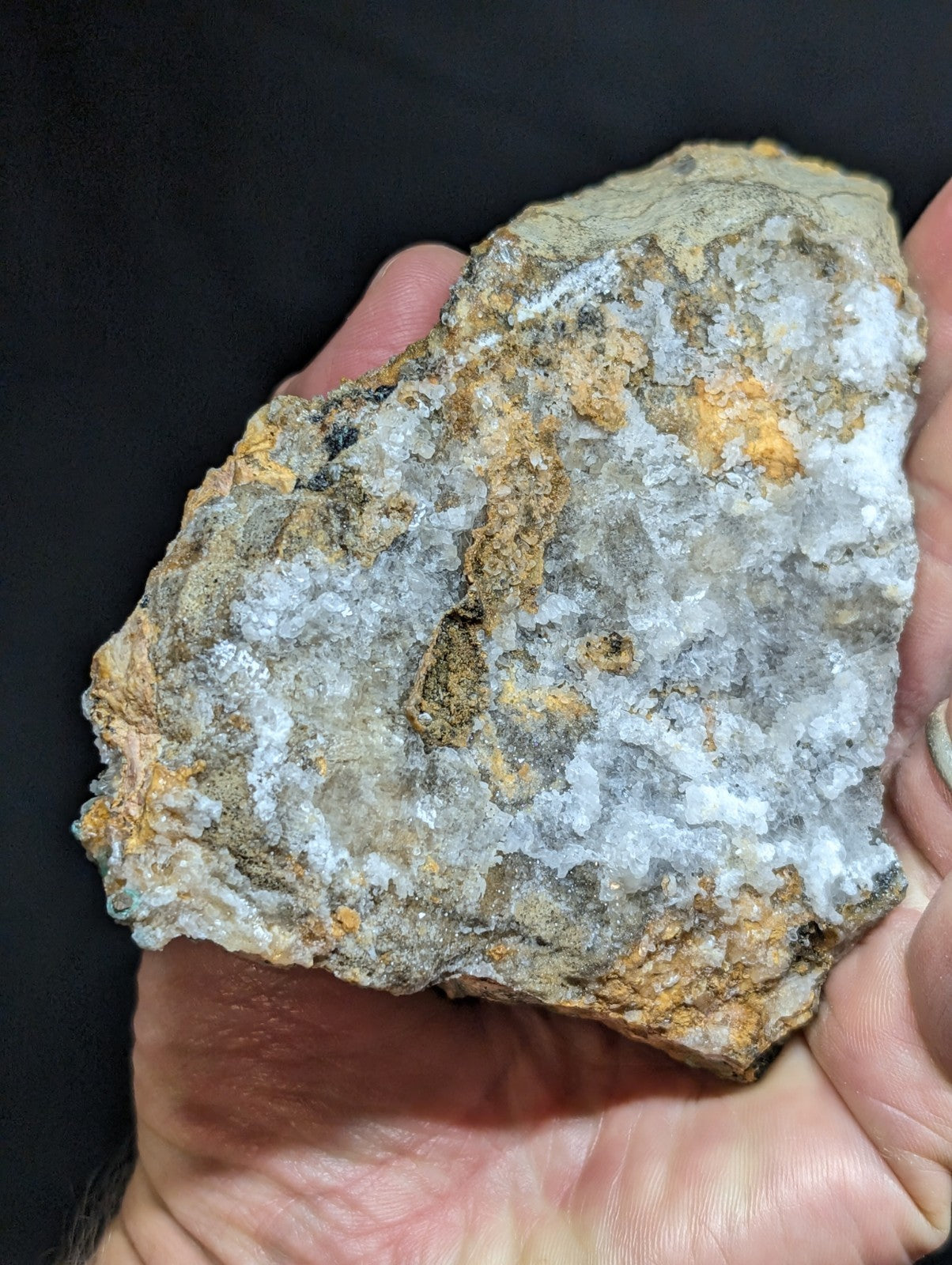 A rugged, irregularly shaped rock with a mottled surface of gray, white crystalline patches and streaks of orange-brown mineral veins.