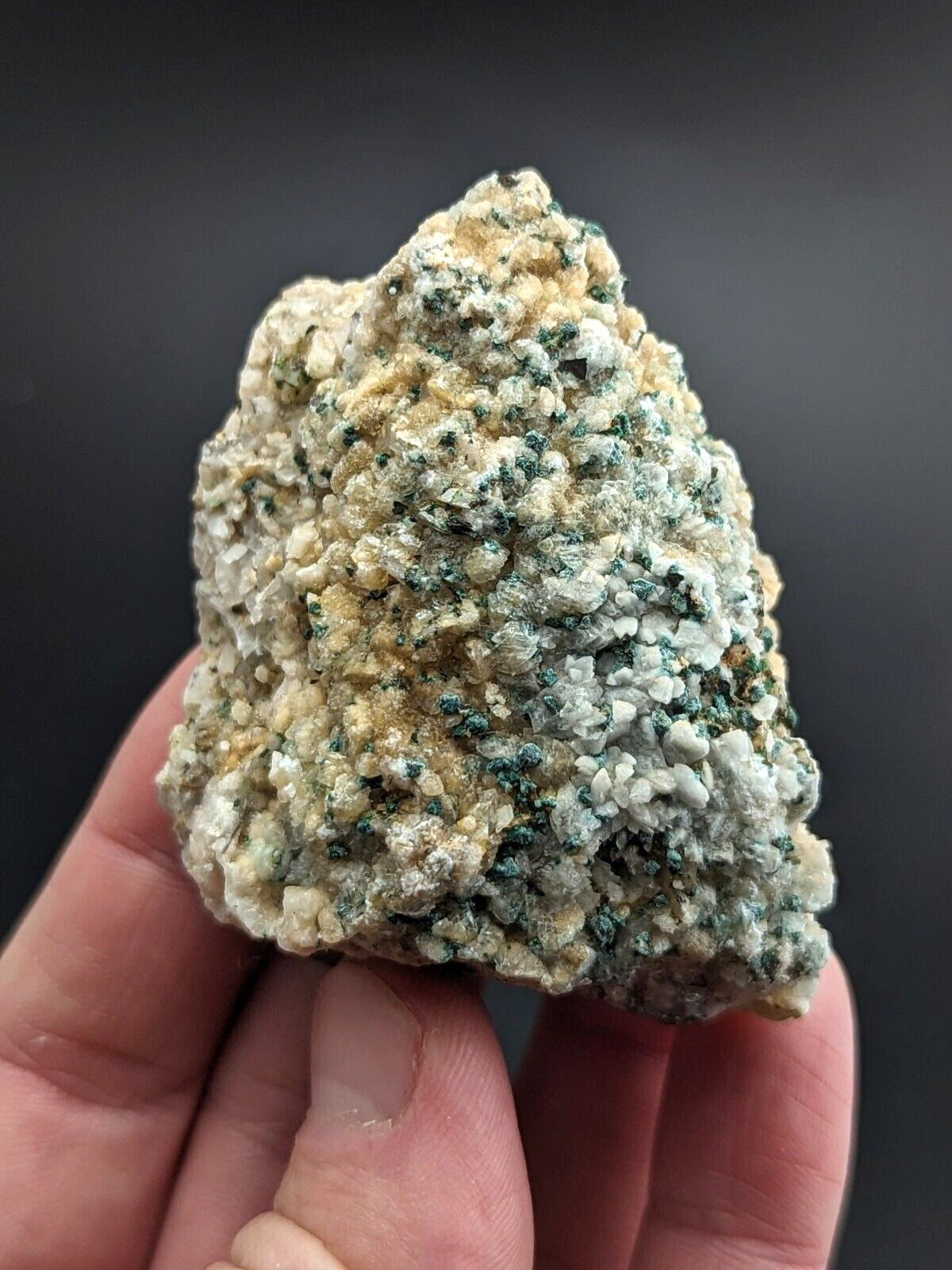 A textured, irregularly shaped mineral specimen with a mottled surface of pale beige and speckles of dark green.