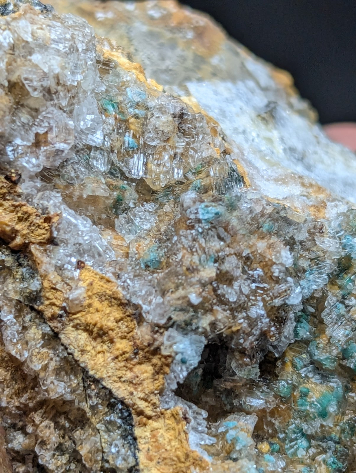 A translucent crystal cluster with clear, faceted formations and patches of vibrant teal mineral embedded in a golden-brown rock matrix.