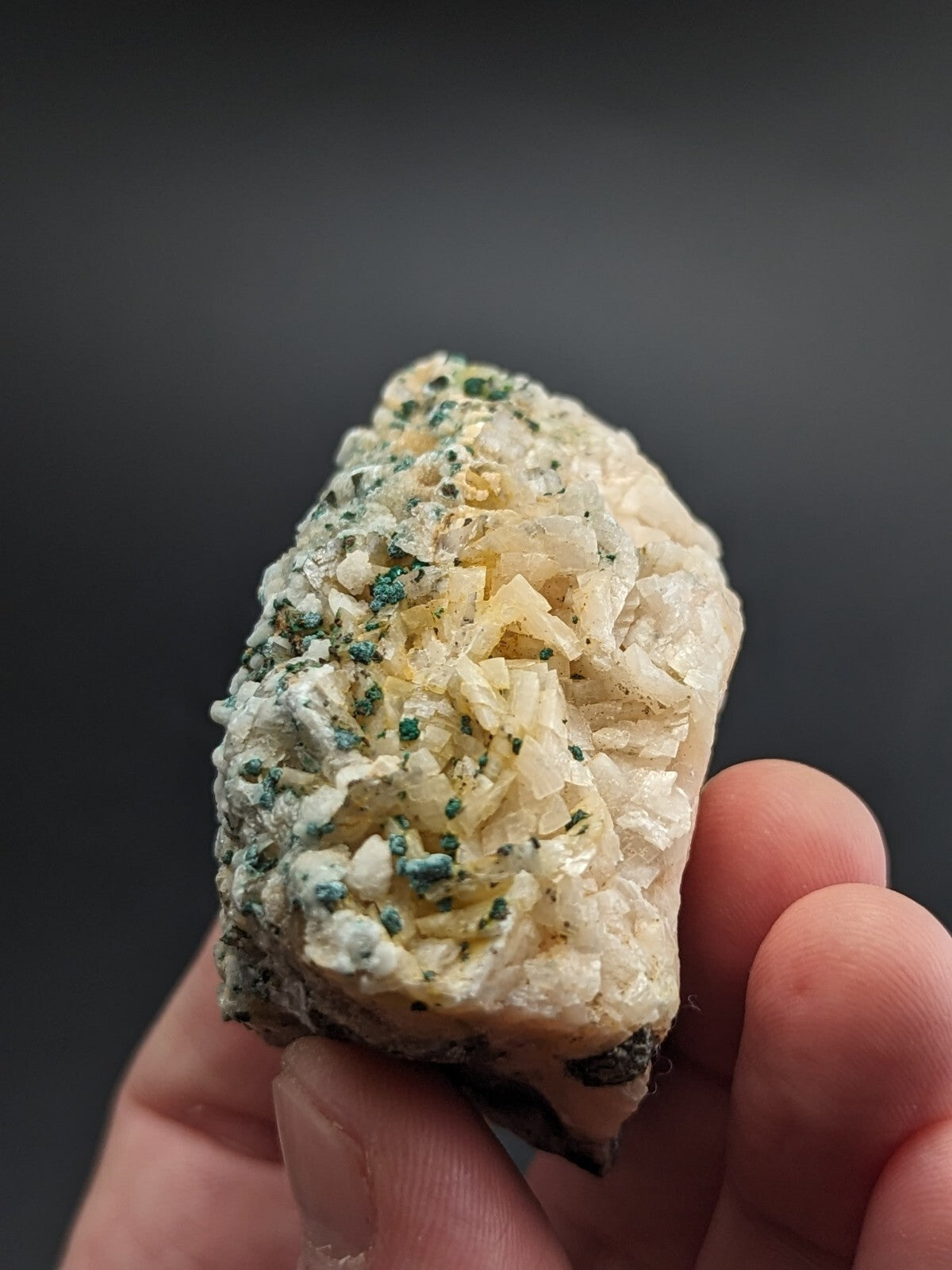 A hand holds a natural mineral specimen featuring translucent, crystalline formations with greenish-blue speckles and yellowish crystals.