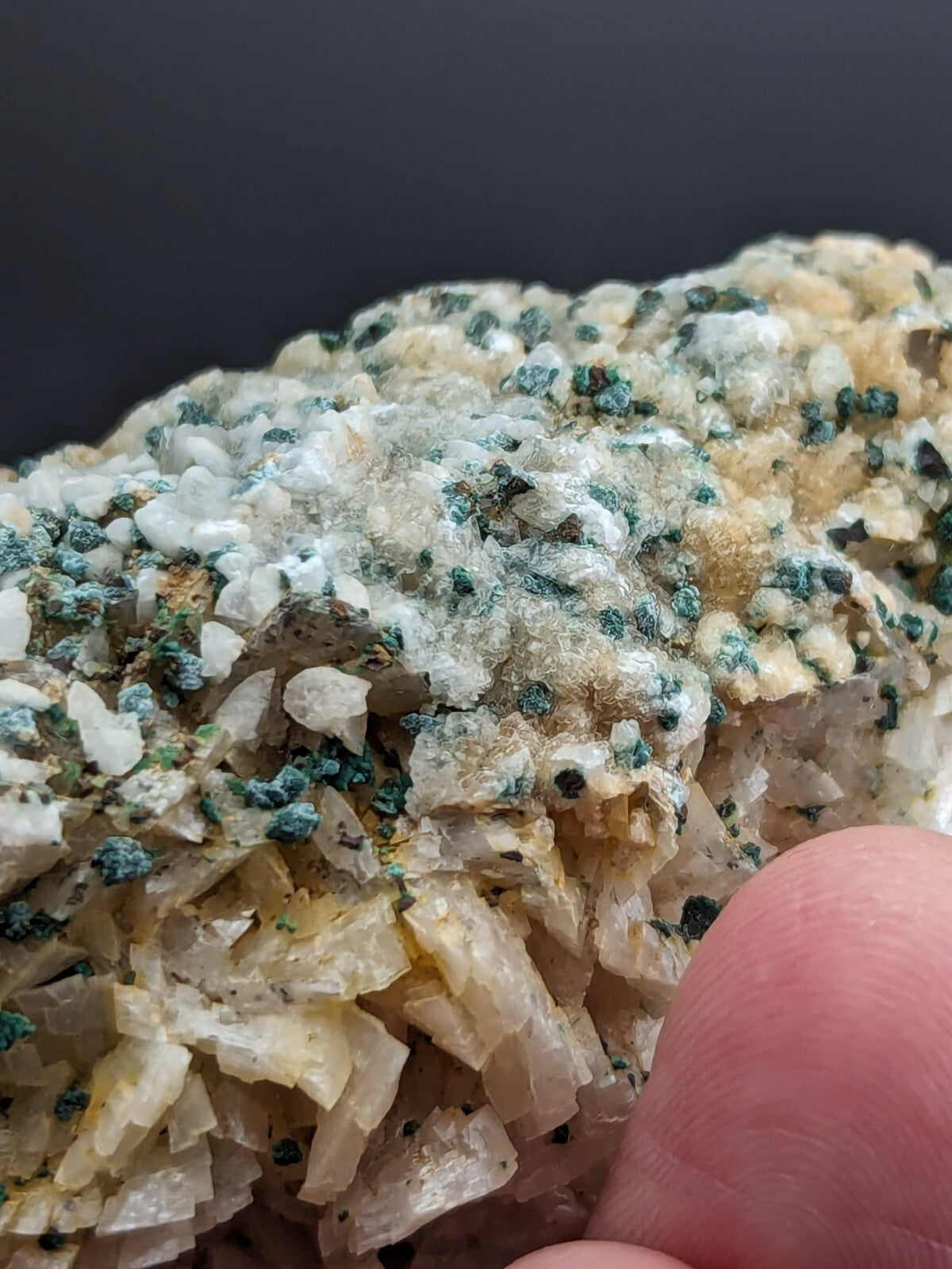 A textured mineral specimen featuring translucent, crystalline formations in shades of white and pale yellow, speckled with patches of greenish-blue crystals.