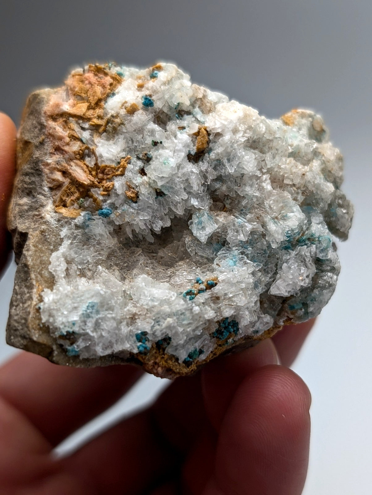 A hand holds a very rare aurichalcite and selenite mineral with white crystals and turquoise patches from Arkansas