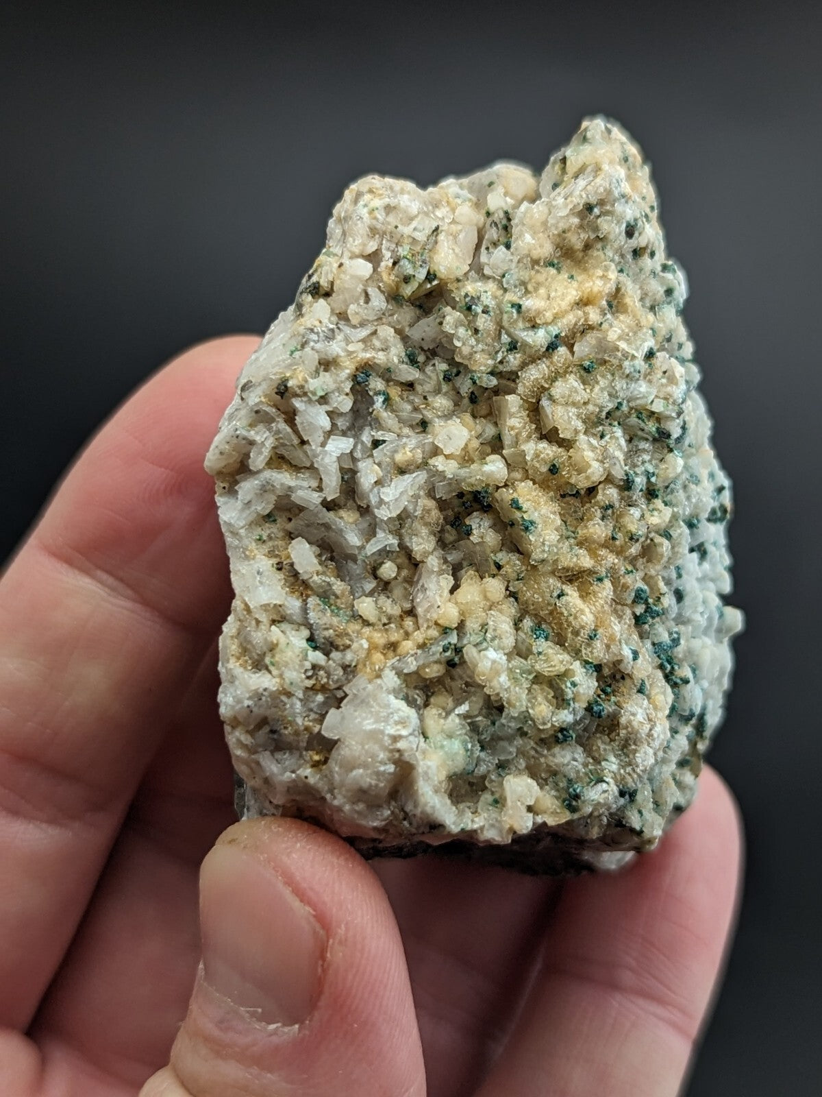 A textured, irregularly shaped mineral specimen with a mix of white and pale yellow crystalline formations interspersed with specks of green.