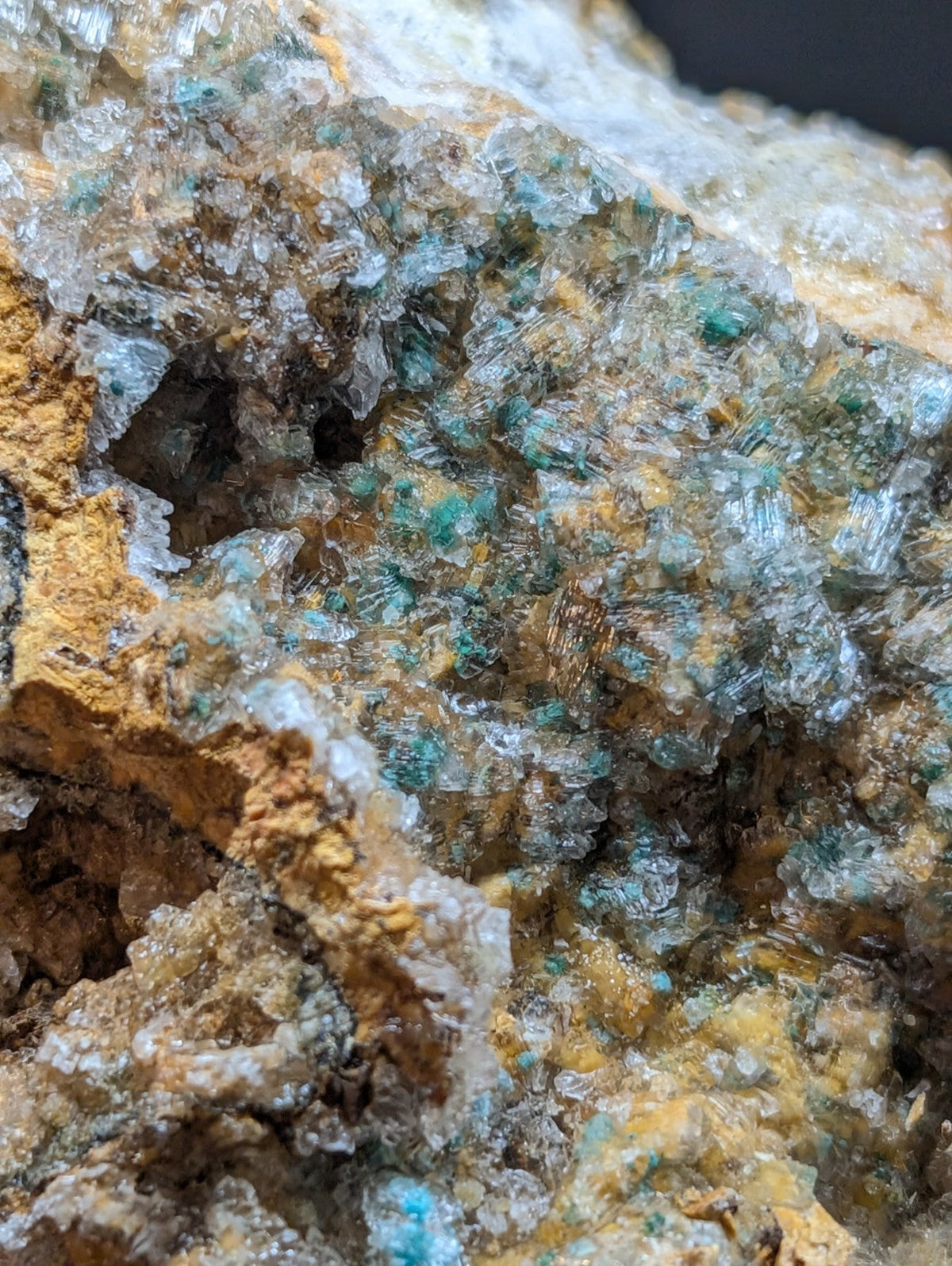 A cluster of translucent turquoise and clear crystals embedded in a rugged, earthy yellow matrix.