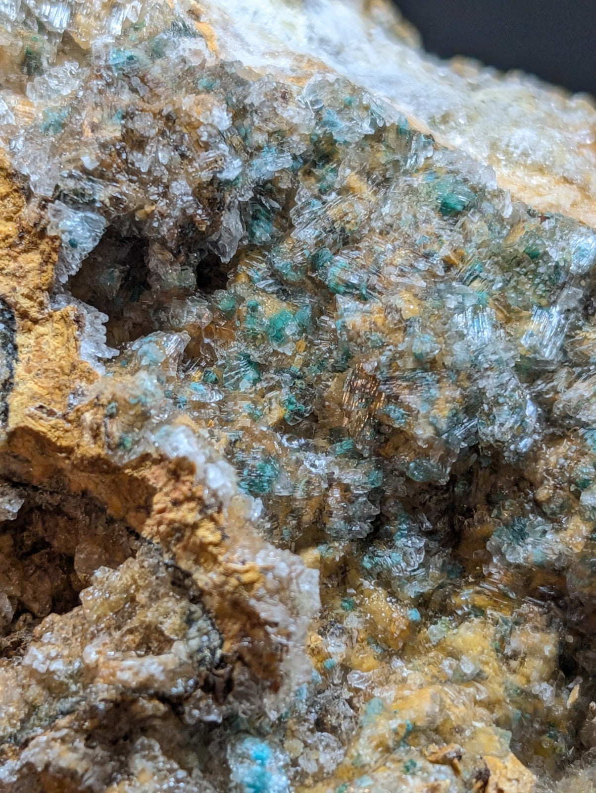 A cluster of translucent turquoise and clear crystals embedded in a rugged, earthy yellow matrix.