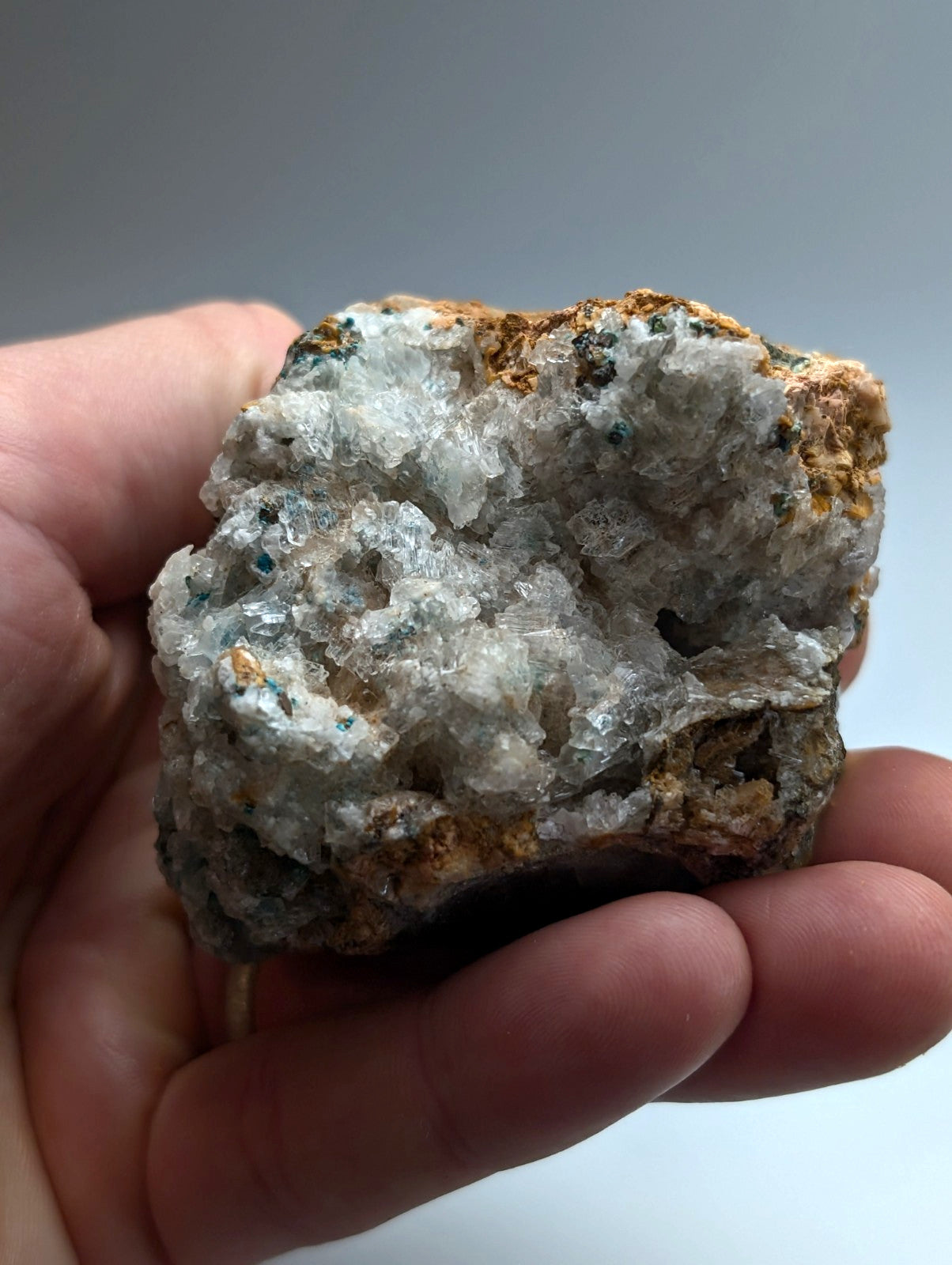 A hand holds a rare aurichalcite and selenite crystal cluster with white gray and brownish orange formations from Arkansas