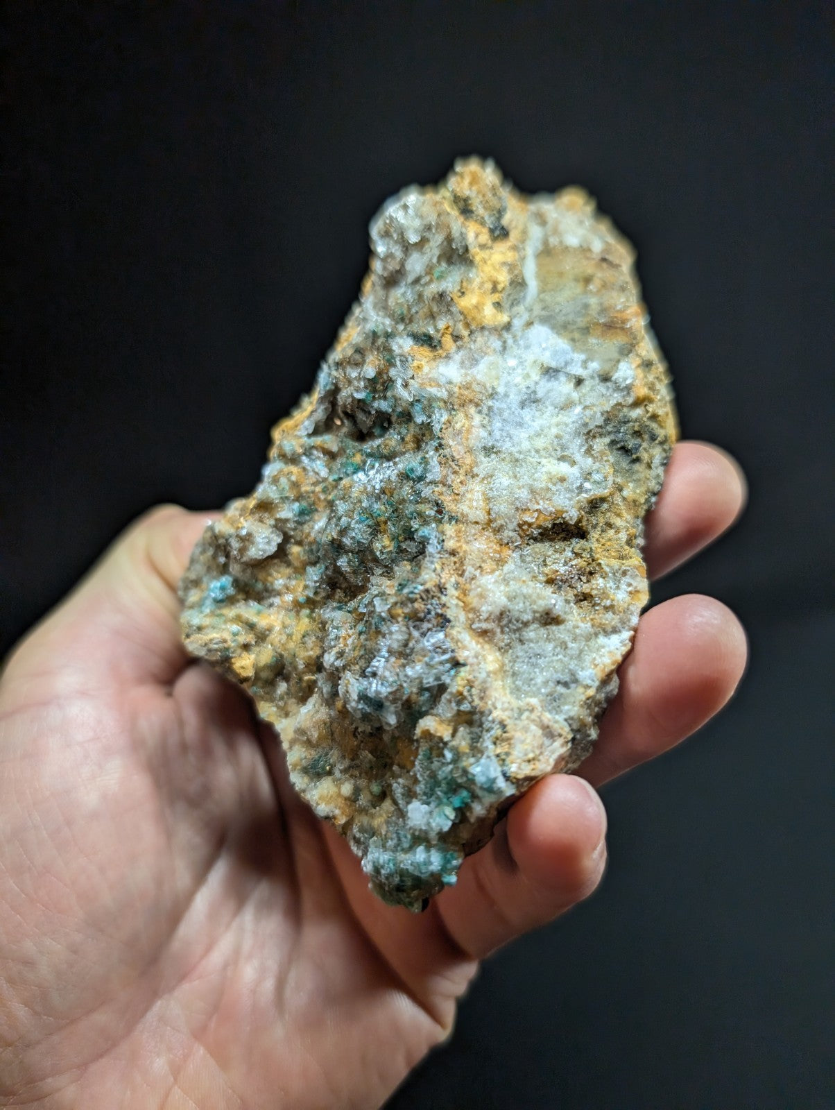 A rugged, irregularly shaped mineral specimen with patches of vibrant turquoise and yellowish-orange hues against a darker matrix.