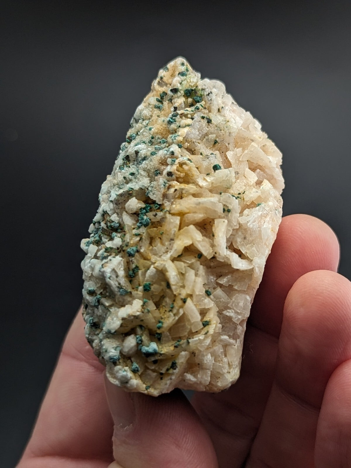 A hand holds a natural mineral specimen featuring translucent white crystals with green and yellowish patches.