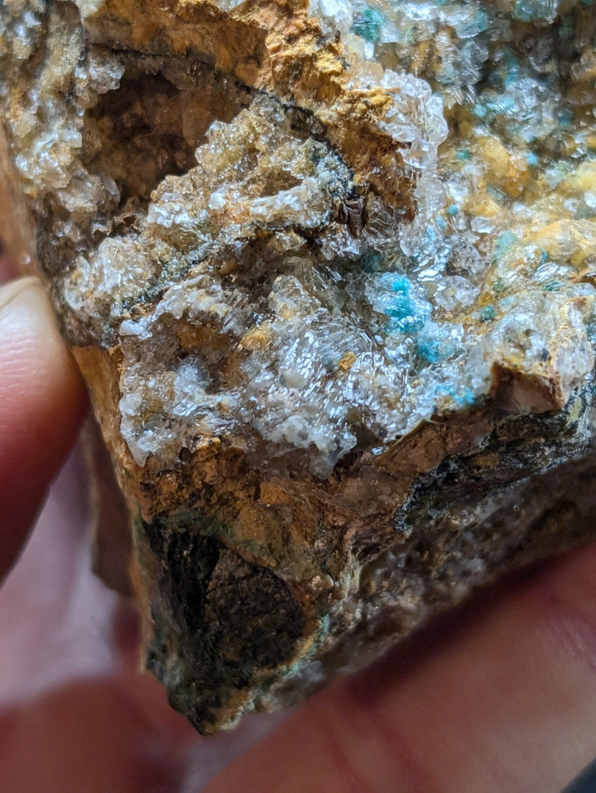 A rugged, naturally occurring mineral specimen featuring translucent crystalline formations with hints of blue and gold against a rough, earthy matrix.