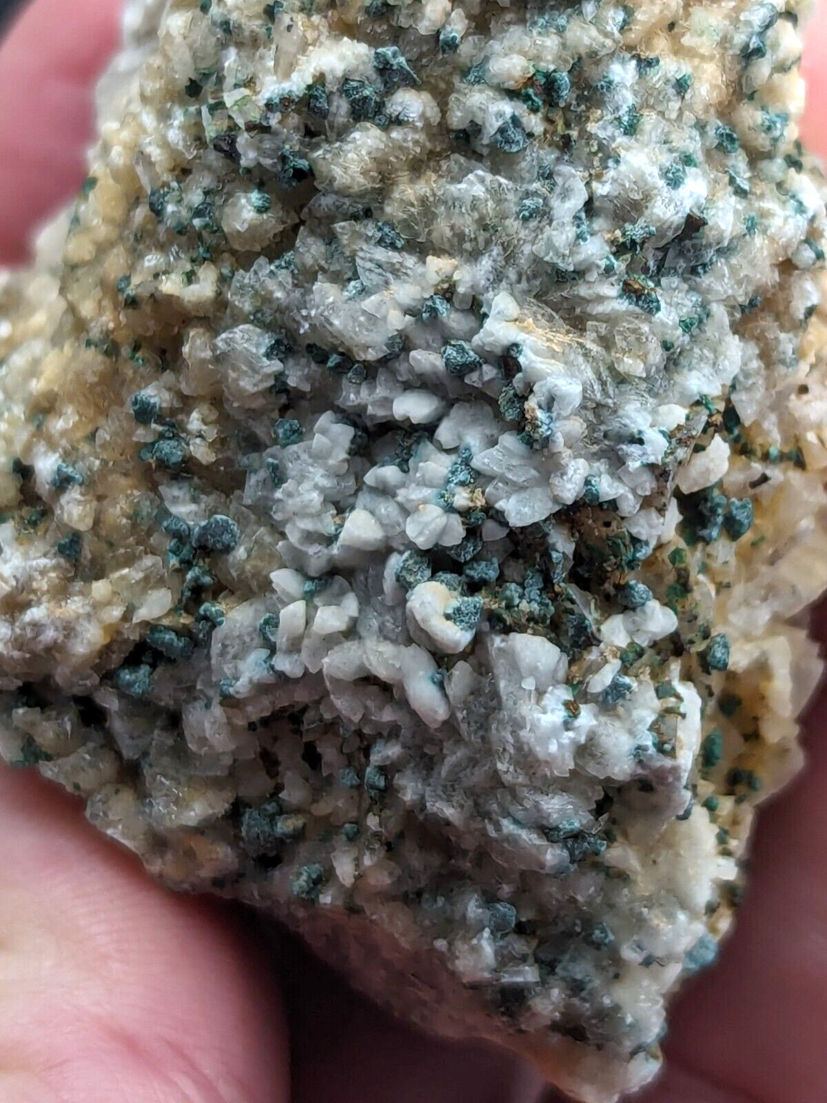 A textured mineral specimen featuring a mix of translucent white crystals and speckles of dark green, set against a pale yellowish matrix.