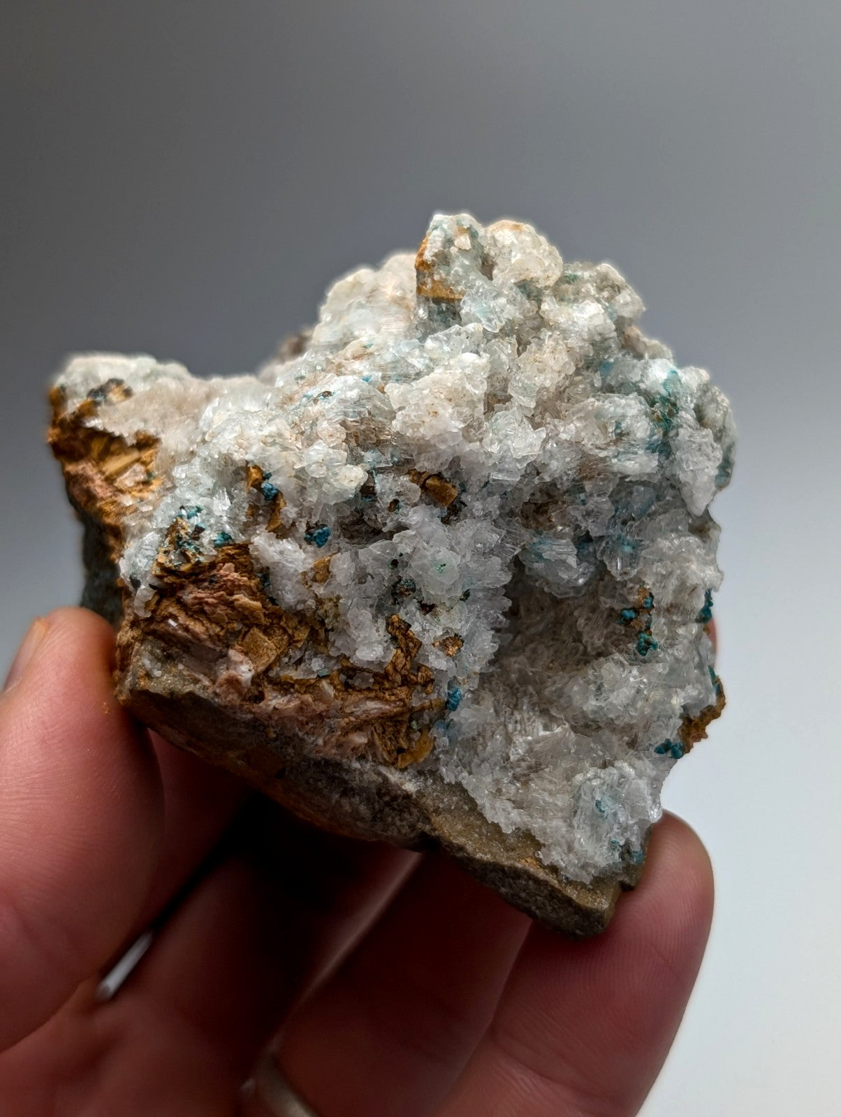 A hand holds a rough aurichalcite and selenite mineral with white crystals and golden brown patches from Arkansas