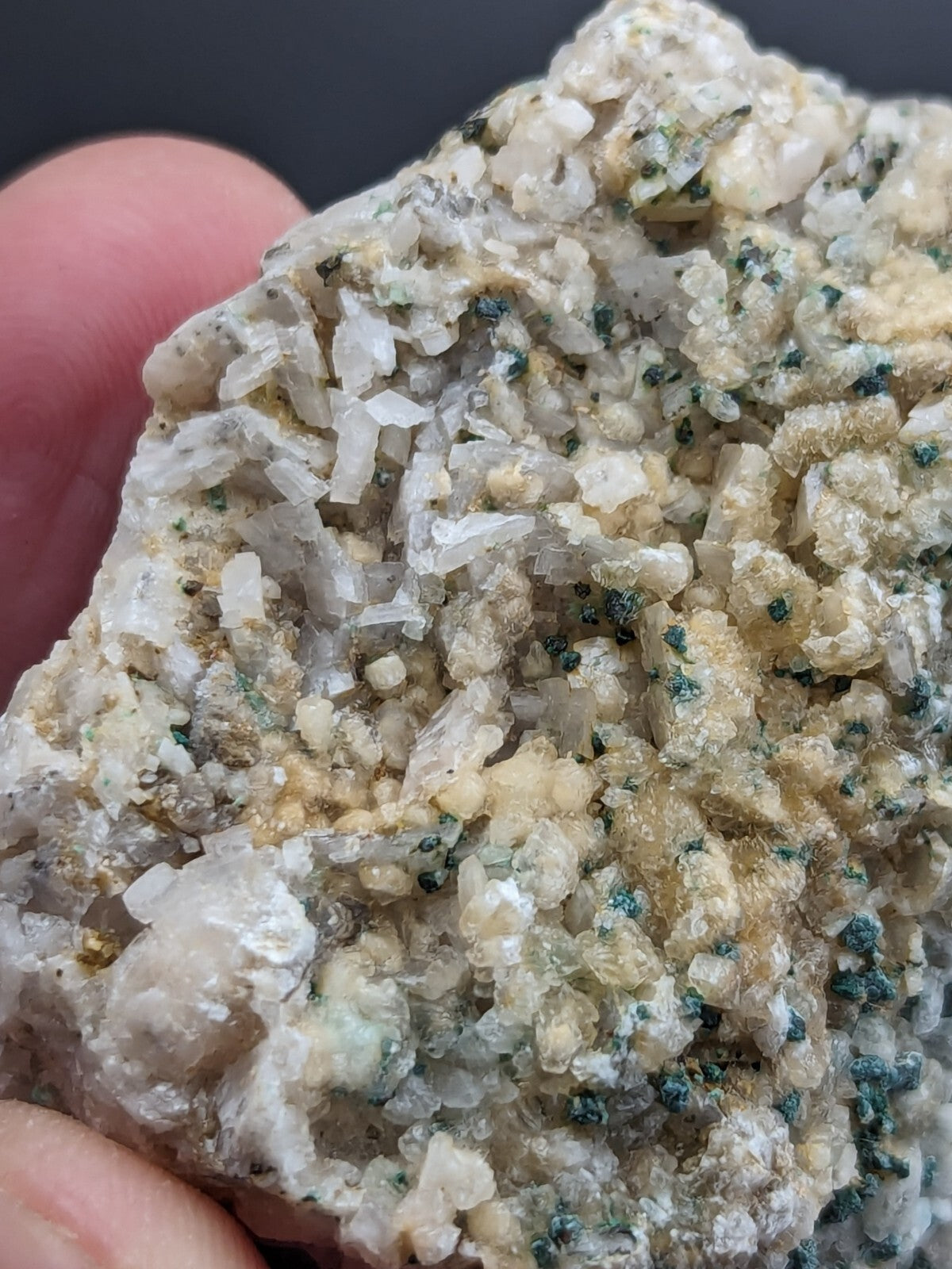 A textured mineral specimen featuring translucent white and pale yellow crystals interspersed with specks of dark green.