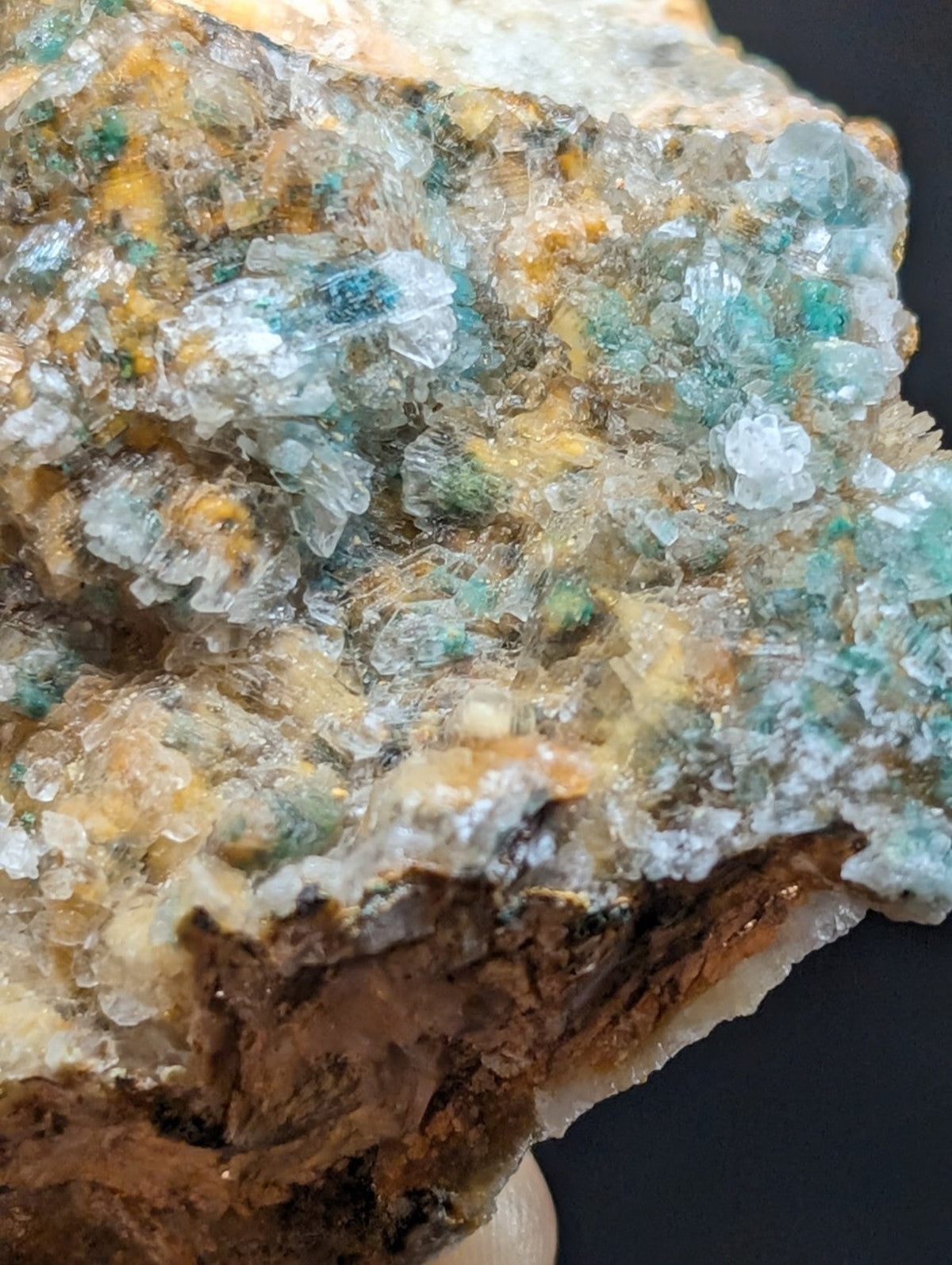 A cluster of translucent turquoise and yellow crystals growing on a rough, earthy matrix.