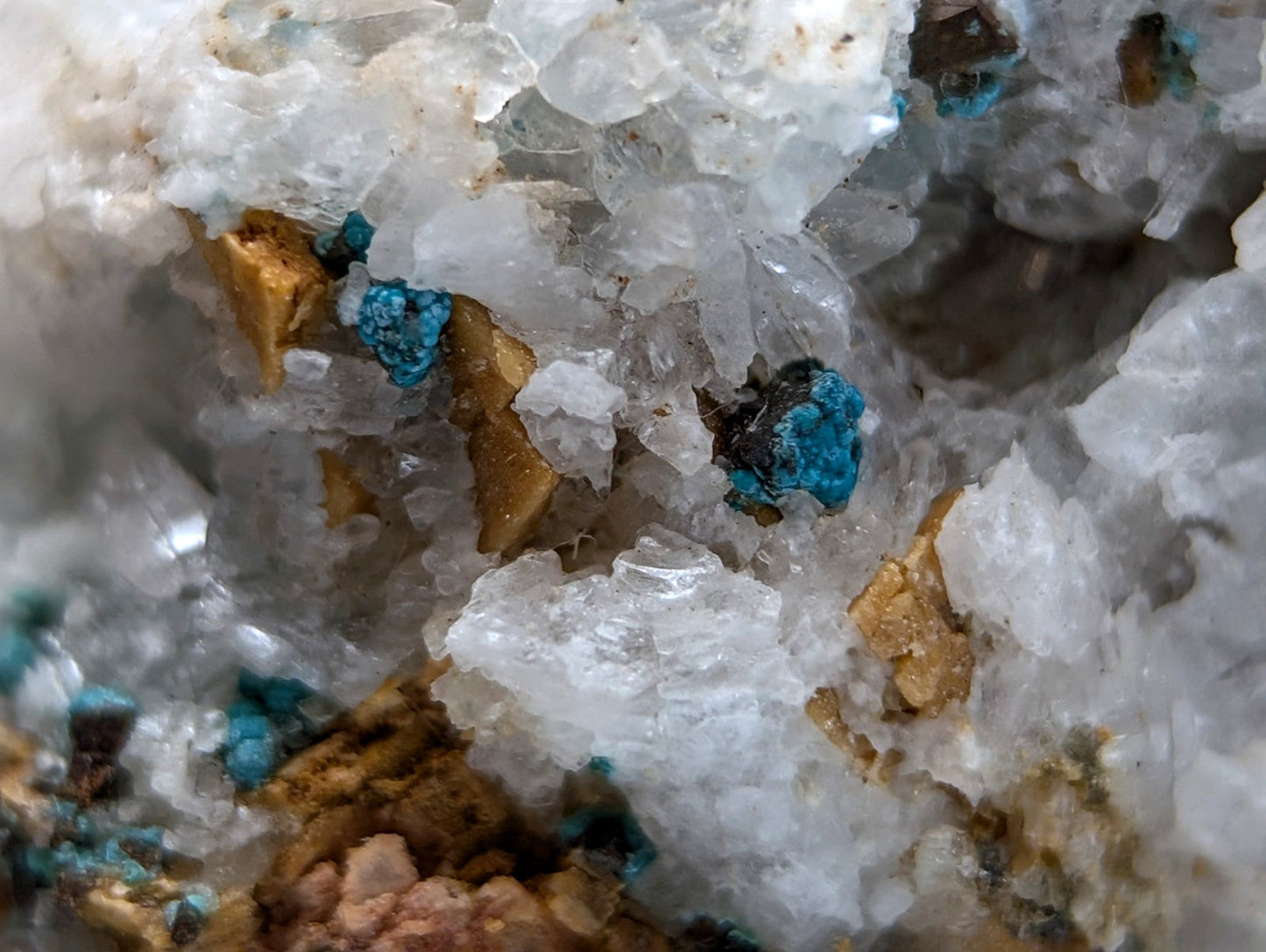 A cluster of translucent white quartz crystals with blue turquoise and golden metallic inclusions from red cloud mine arkansas
