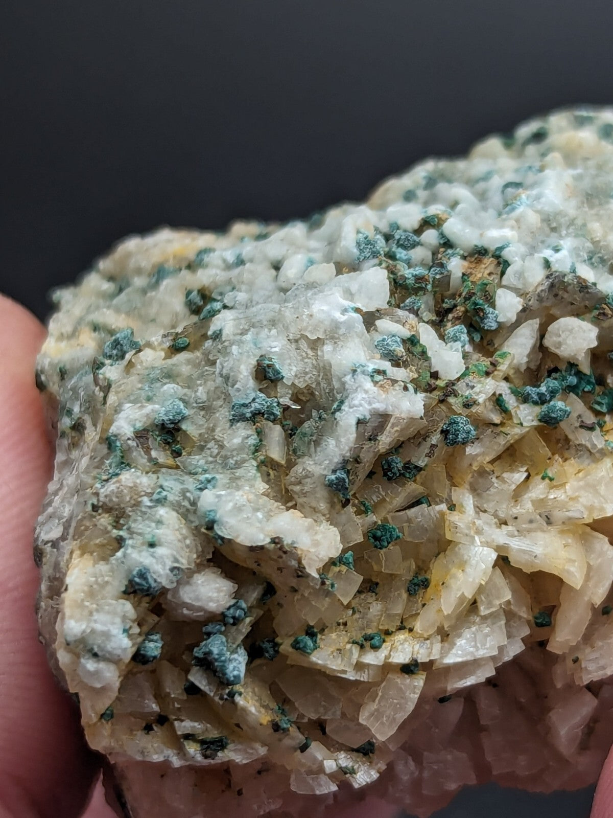 A cluster of translucent, pale yellowish-white crystals with scattered green-blue mineral inclusions.