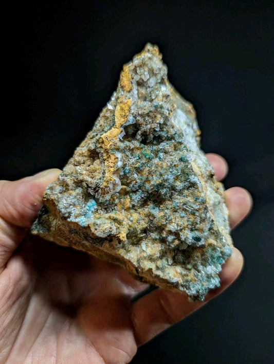 A rugged, triangular mineral specimen with a textured surface featuring patches of vibrant turquoise and earthy yellow-orange hues.