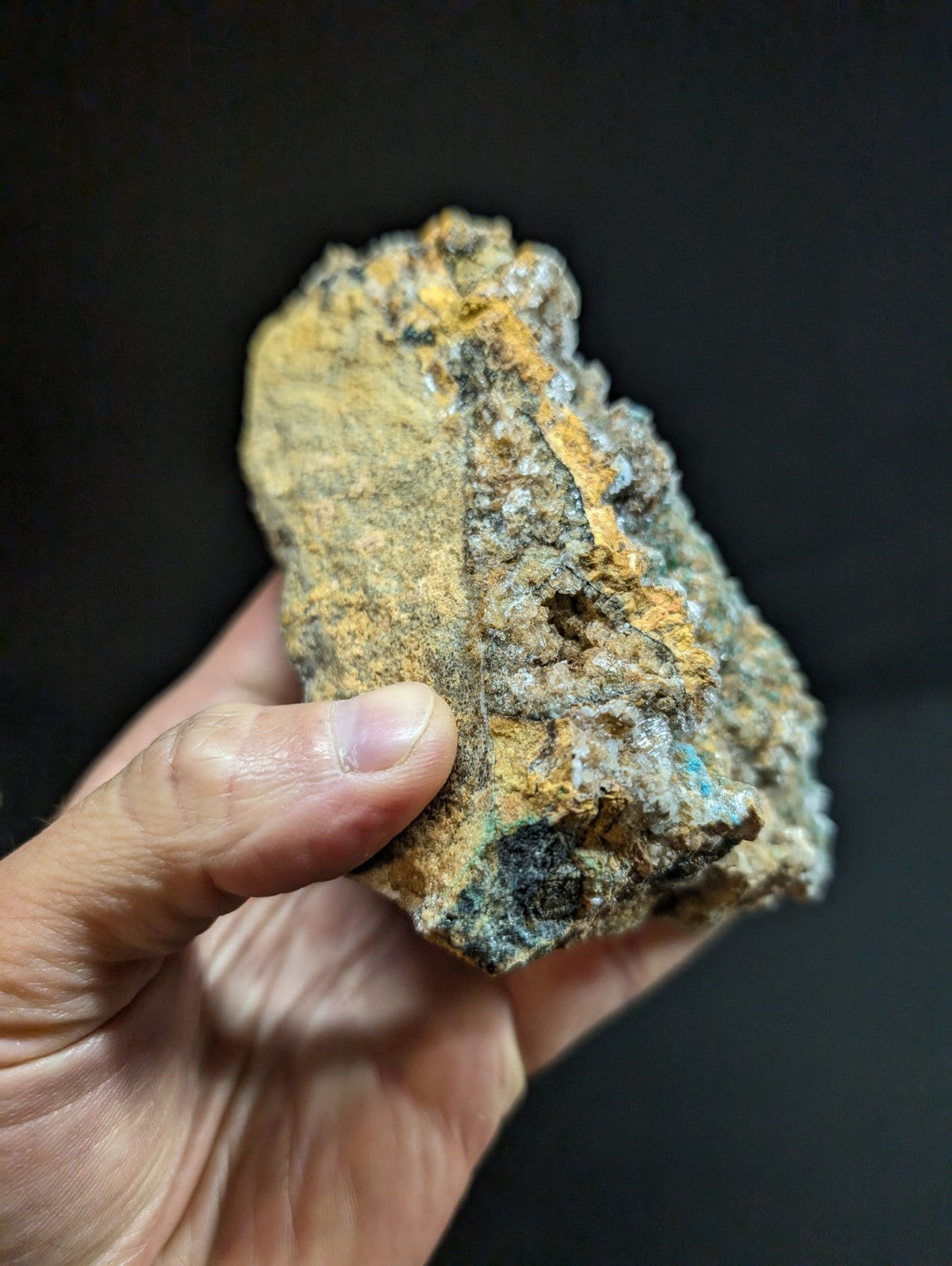 A rugged, irregularly shaped mineral specimen with a textured surface displaying patches of yellowish-orange and dark green-blue hues.