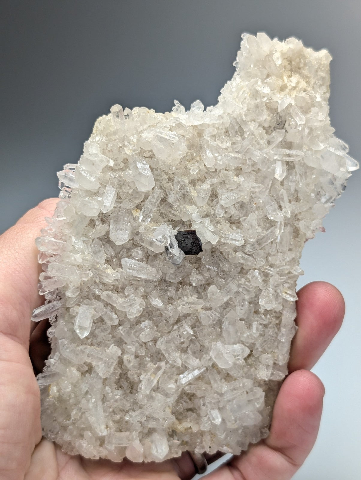 A hand holds a translucent crystalline quartz geode with clear jagged crystals from Miller Mountain Arkansas