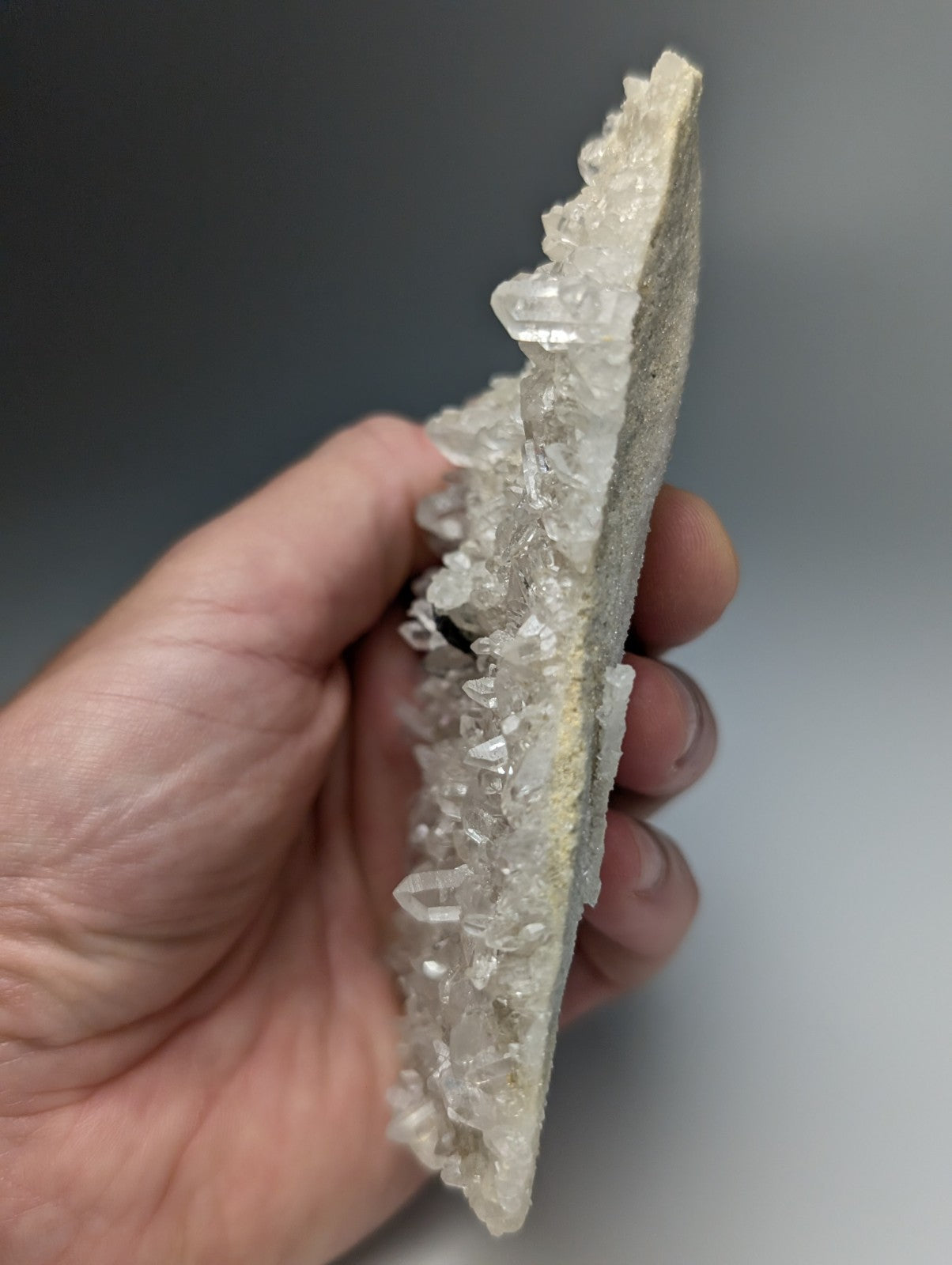 A hand holds a very rare brookite on quartz geode with sharp clear crystals from Miller Mountain Arkansas USA