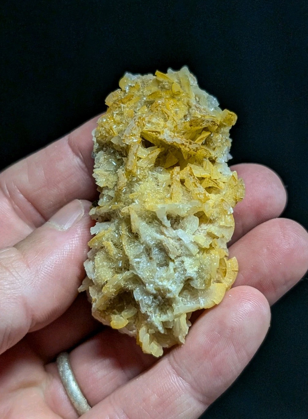 A hand holds a cluster of golden-yellow and pale gray mineral crystals with jagged, translucent edges.