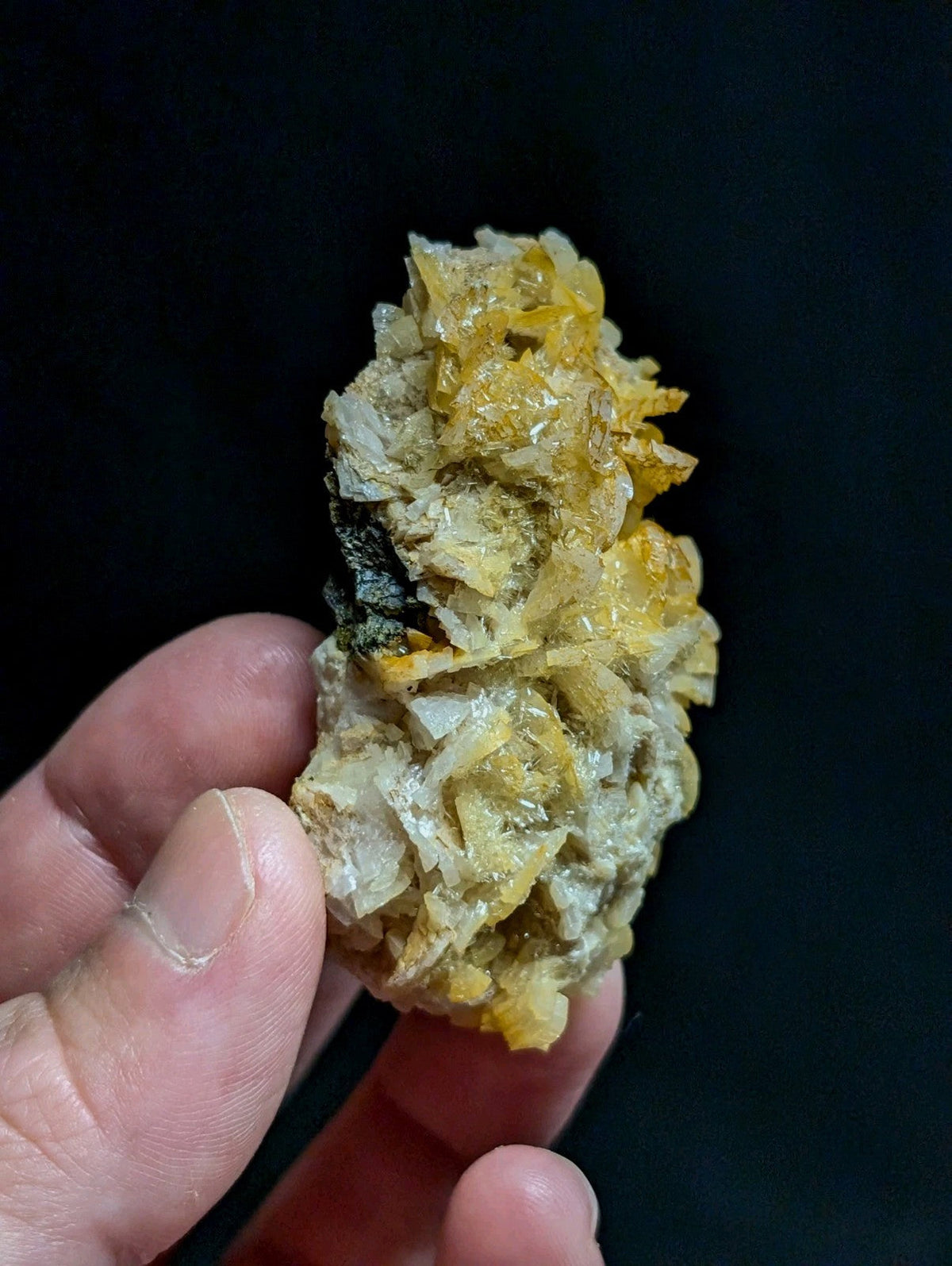 A hand holds a cluster of vibrant yellow and translucent crystals growing from a pale, textured matrix.