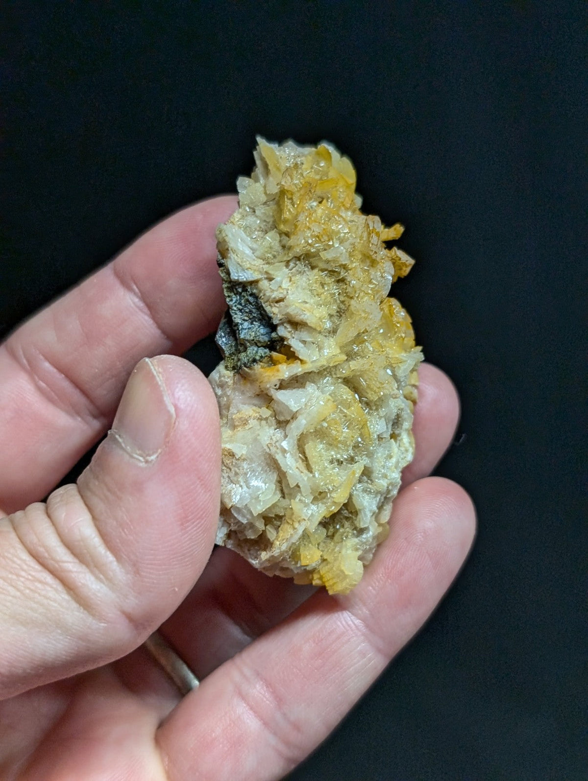 A hand holds a rough, irregularly shaped mineral specimen featuring translucent white crystals intermingled with vibrant yellow and dark gray patches.