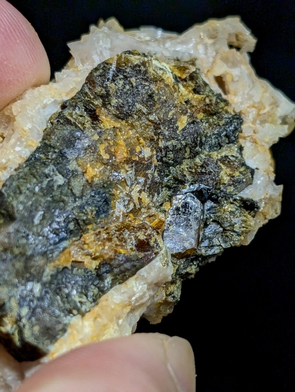A rugged, multi-toned mineral specimen with dark green and black patches accented by golden-yellow streaks, set against a translucent white crystalline matrix.
