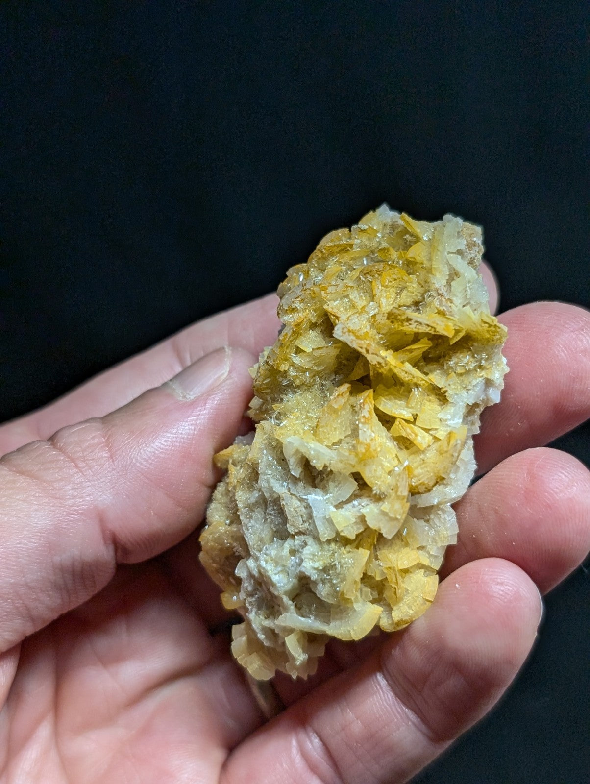 A hand holds a cluster of translucent yellow and white mineral crystals with jagged, interlocking facets.