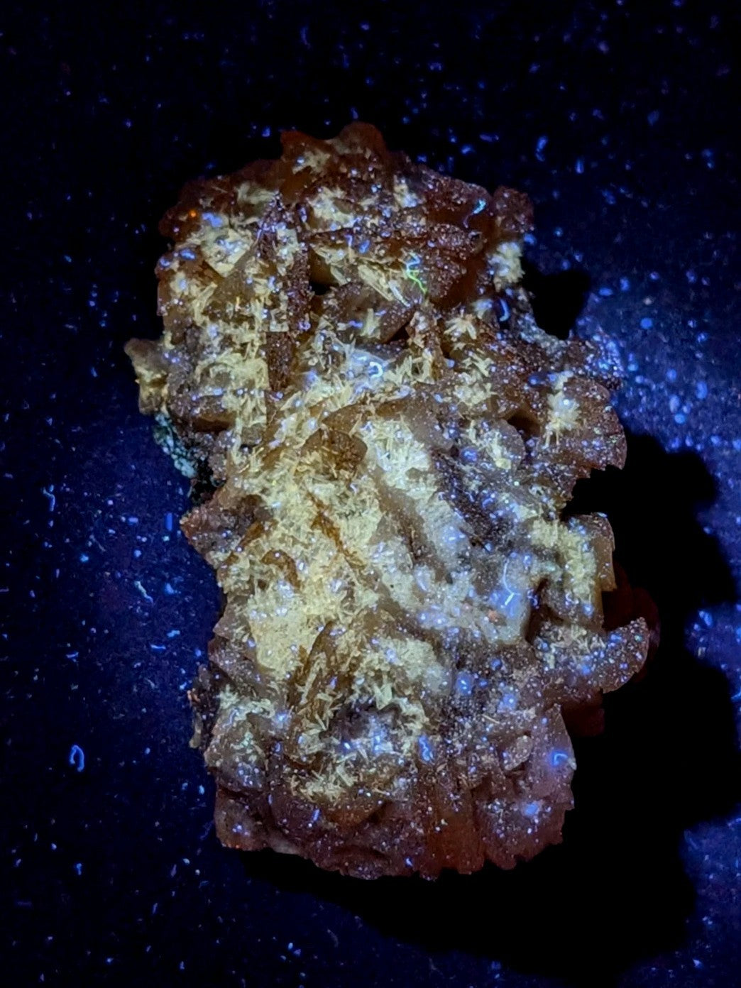 A translucent amber-colored mineral specimen with a rough, crystalline texture and embedded golden-yellow crystals.