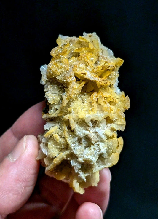 A hand holds a cluster of translucent yellow and white crystalline minerals with jagged, interlocking formations.