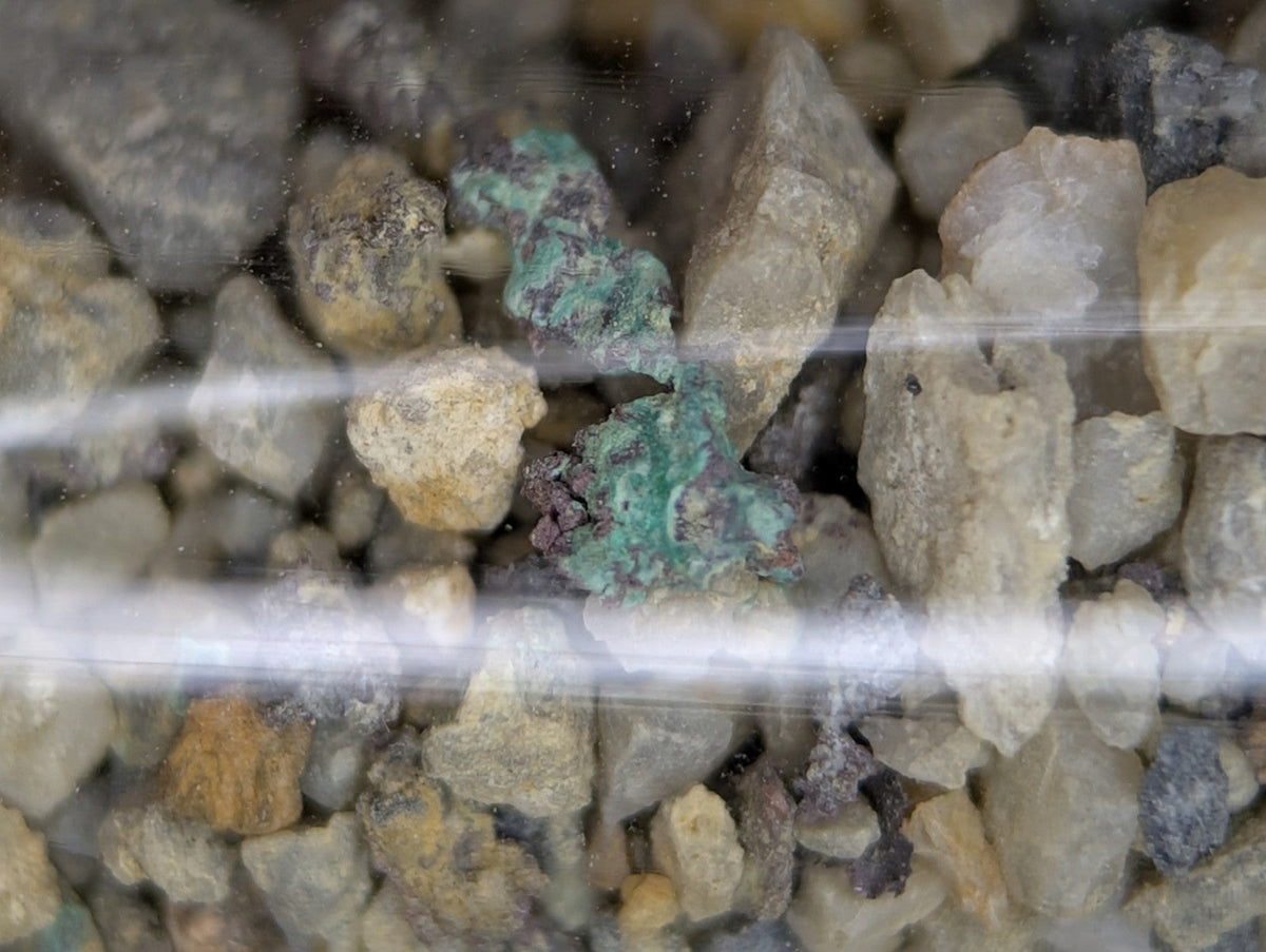A green, textured copper nugget nestled among gray and beige gravel.