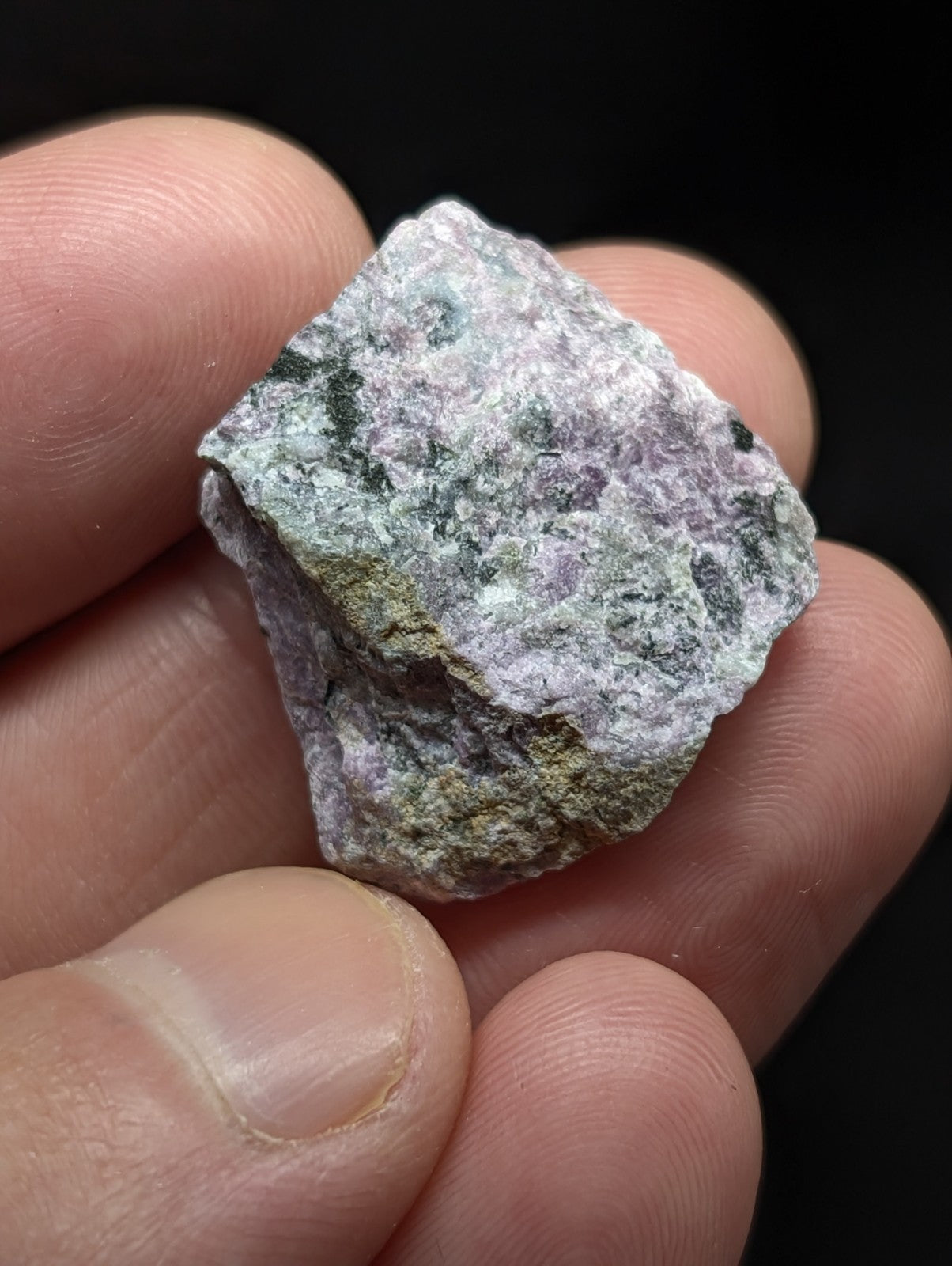 A rough, irregularly shaped mineral specimen with a mottled surface of pale lavender and green hues.