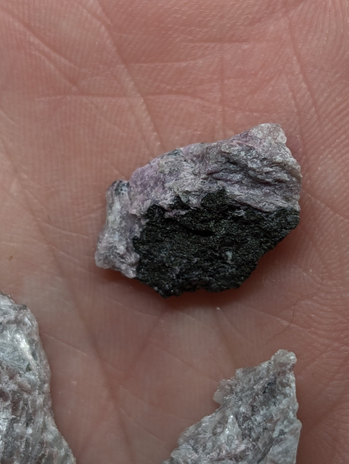 A rough, irregularly shaped mineral specimen with a dark gray to black core and lighter purple-gray outer layers.