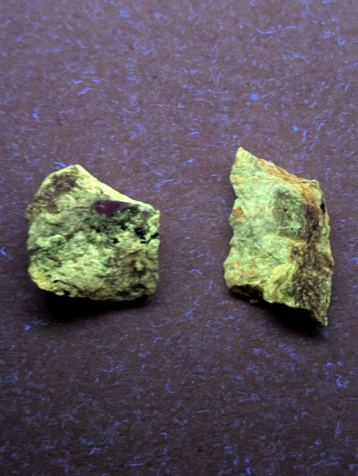 Two irregularly shaped, rough-textured mineral specimens with a predominant greenish-yellow hue and patches of darker brown or black material.