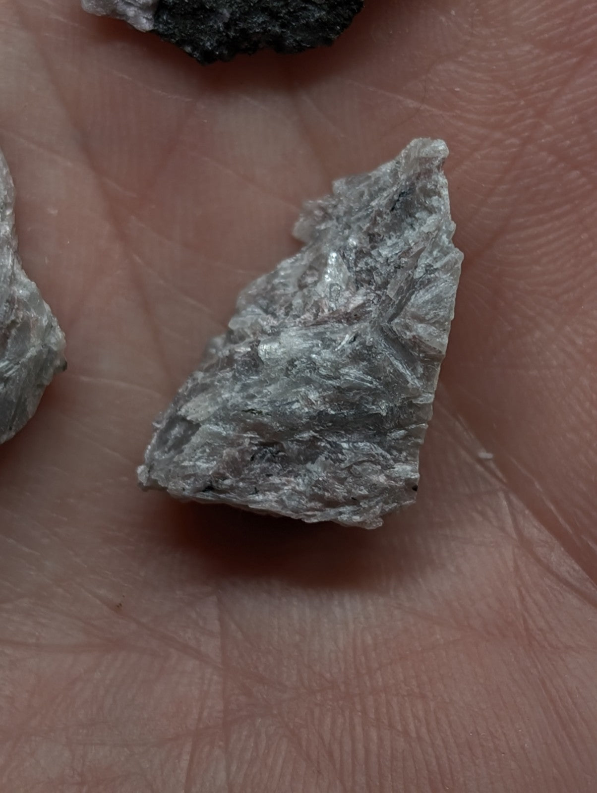 A rough, grayish-white mineral fragment with a crystalline texture and jagged edges.