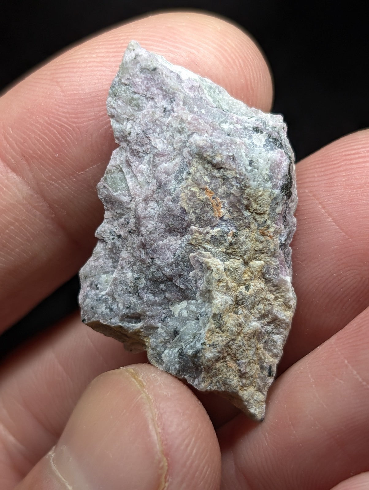 A rough, irregularly shaped mineral specimen with a mottled green and gray surface held in someone’s hand.