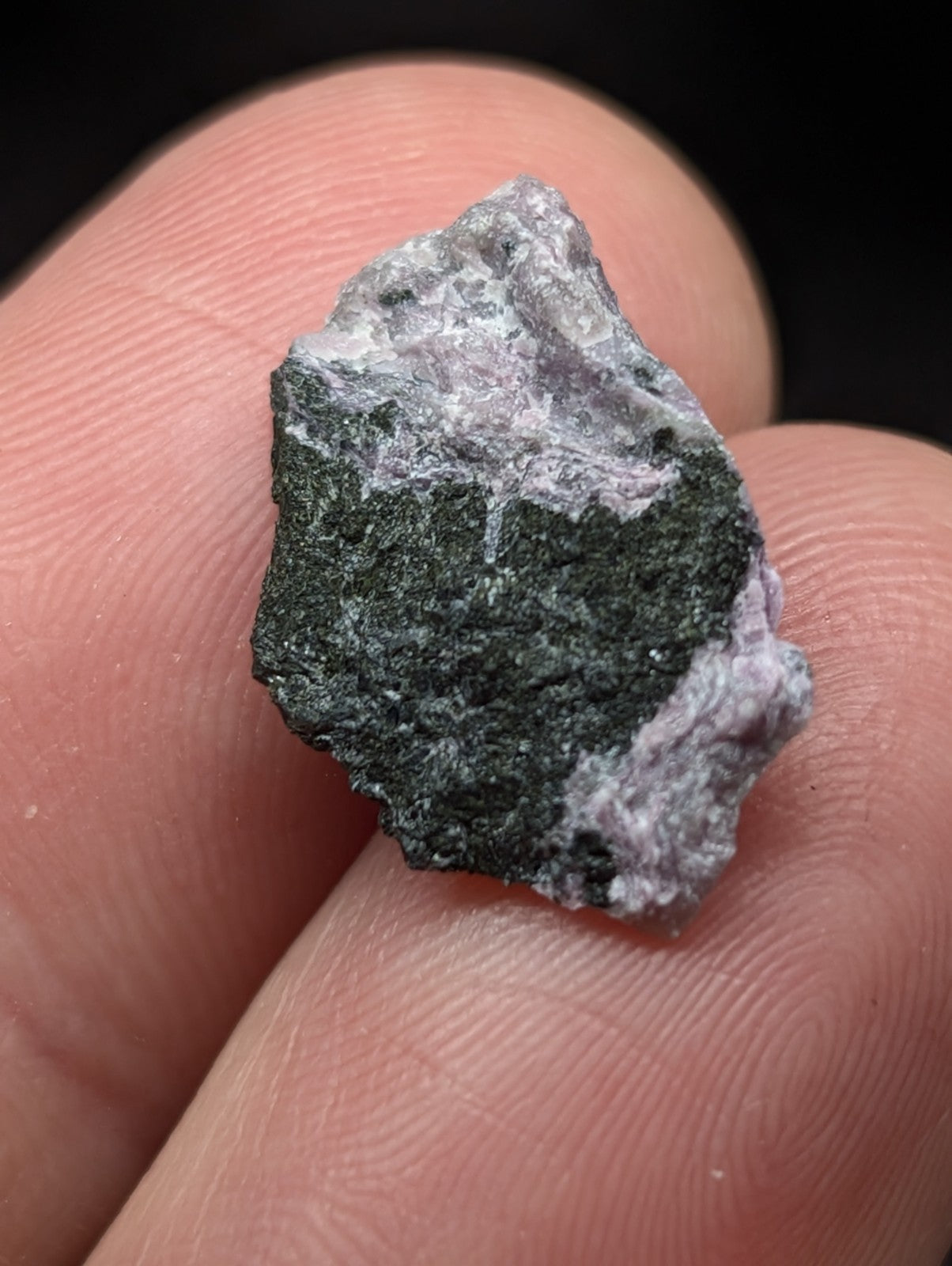 A rough, irregularly shaped mineral specimen with a dark green core and lighter grayish-purple outer layers.
