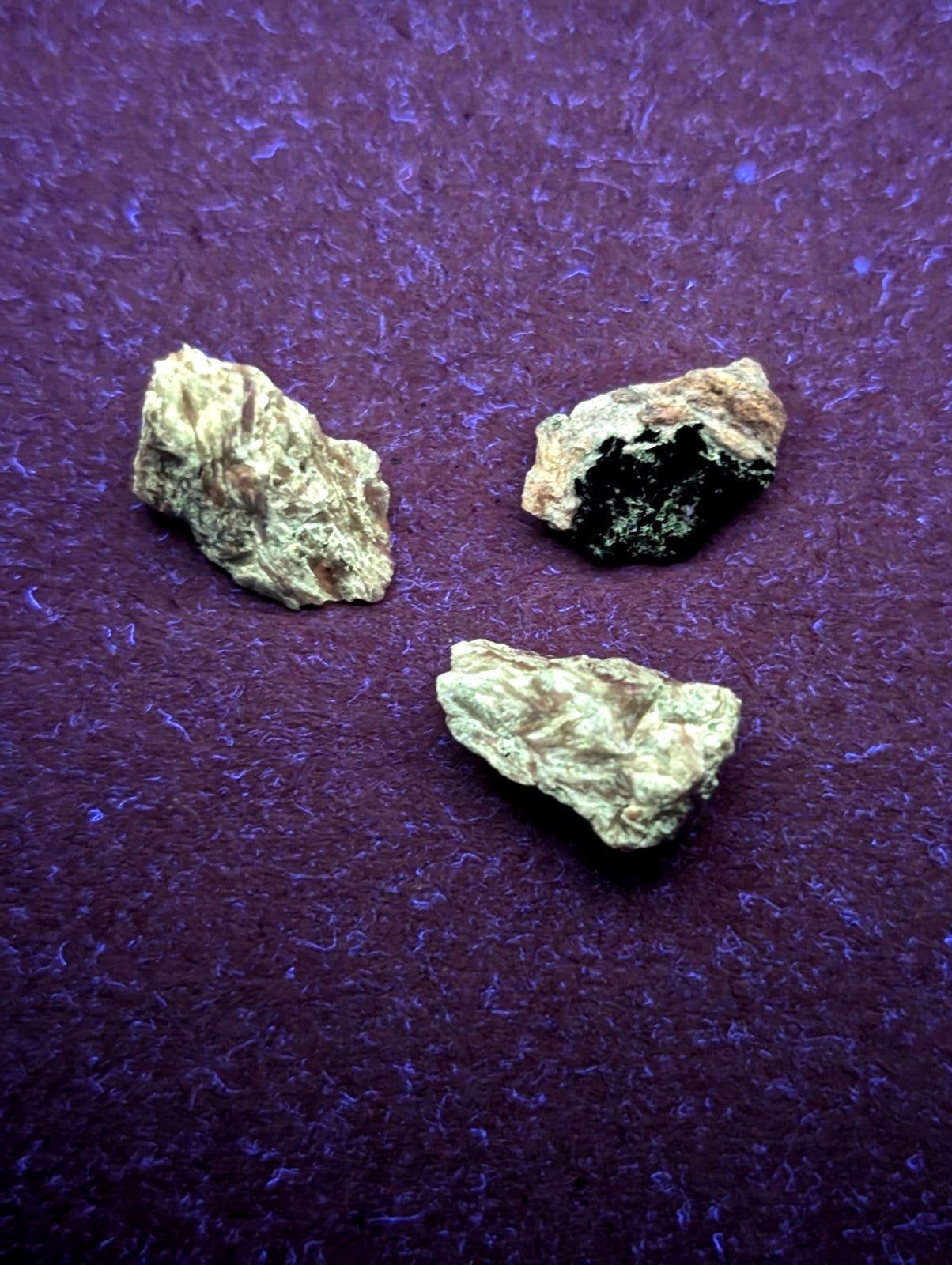 Three irregularly shaped, rough-textured mineral specimens with earthy tones of beige and greenish-gray, one featuring a dark black interior.