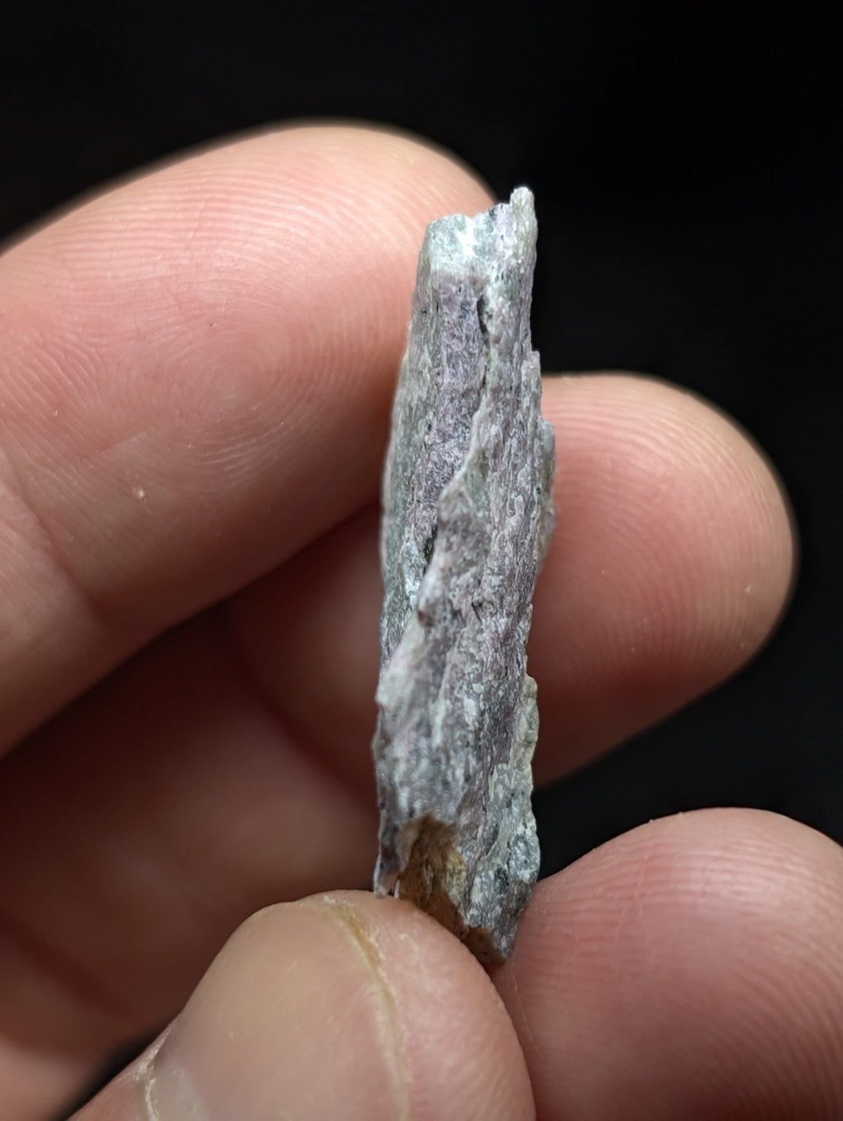 A rough, grayish-green mineral specimen with a jagged edge and visible crystalline texture.